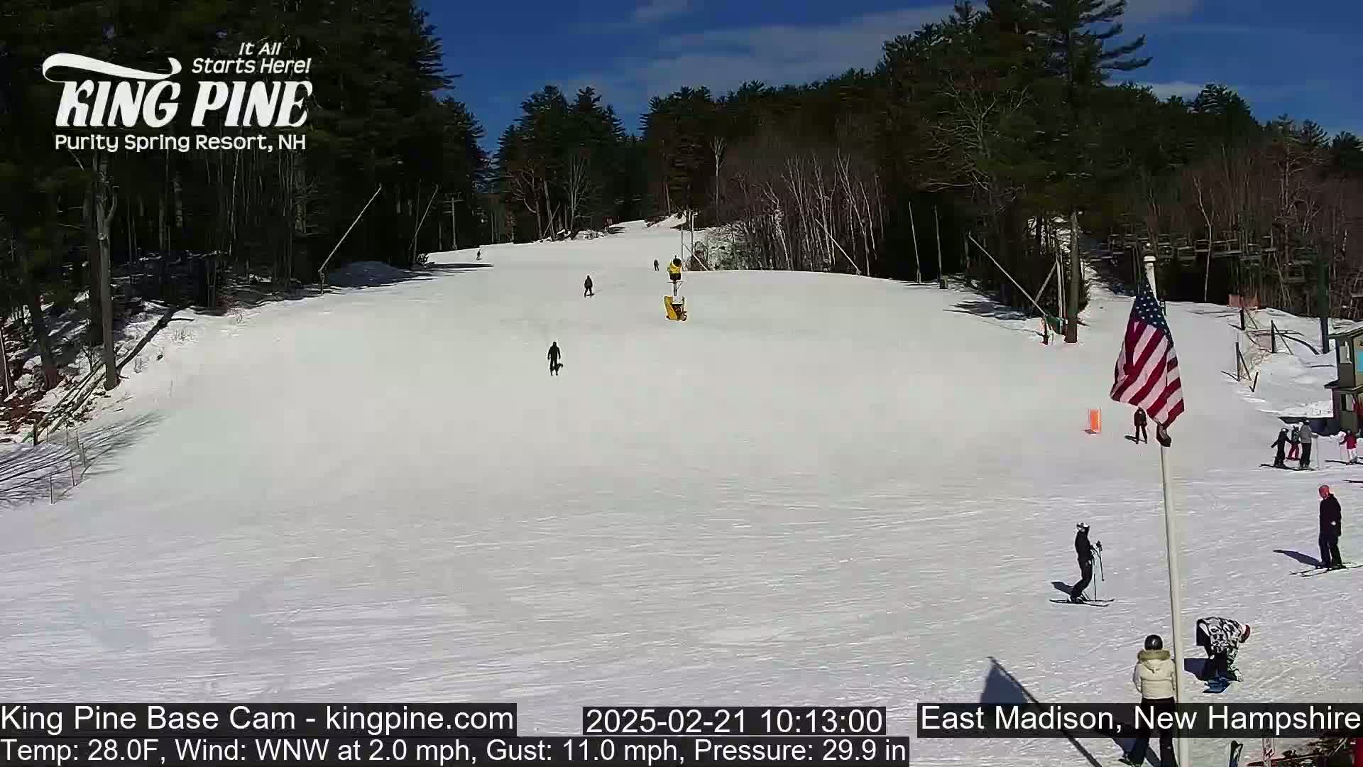 A snow-covered ski slope with several skiers and snowboarders on a sunny day.