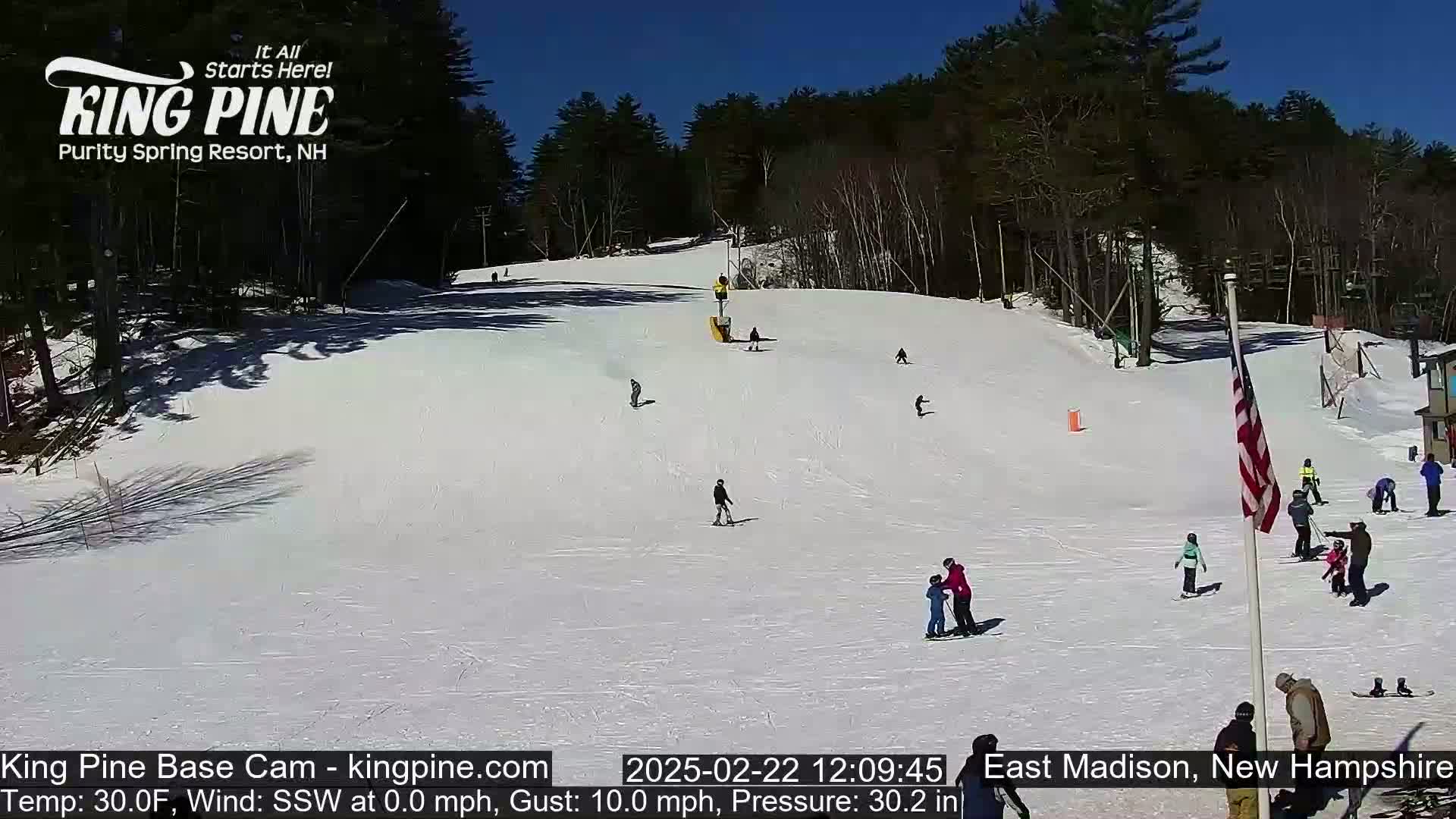 A snow-covered ski slope with several skiers and snowboarders on a sunny day.
