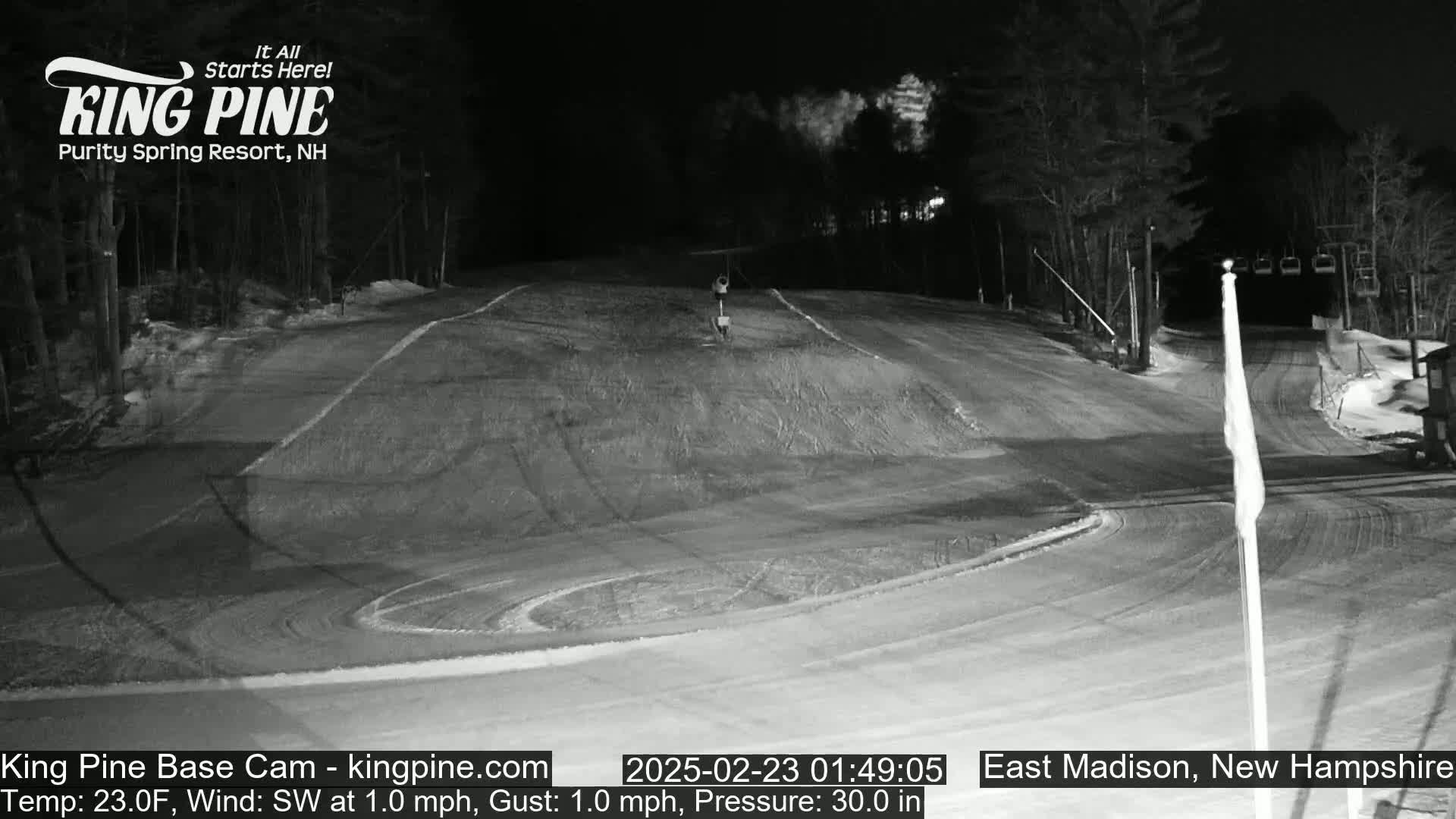 A nighttime view of a snow-covered ski slope with a chairlift in the background under a clear, dark sky.