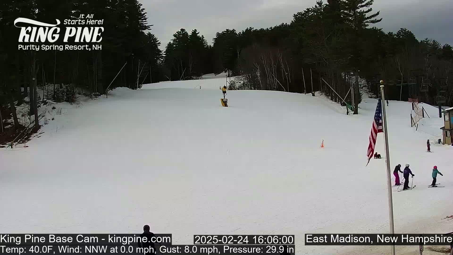 A snow-covered ski slope with several skiers and a partially cloudy sky.