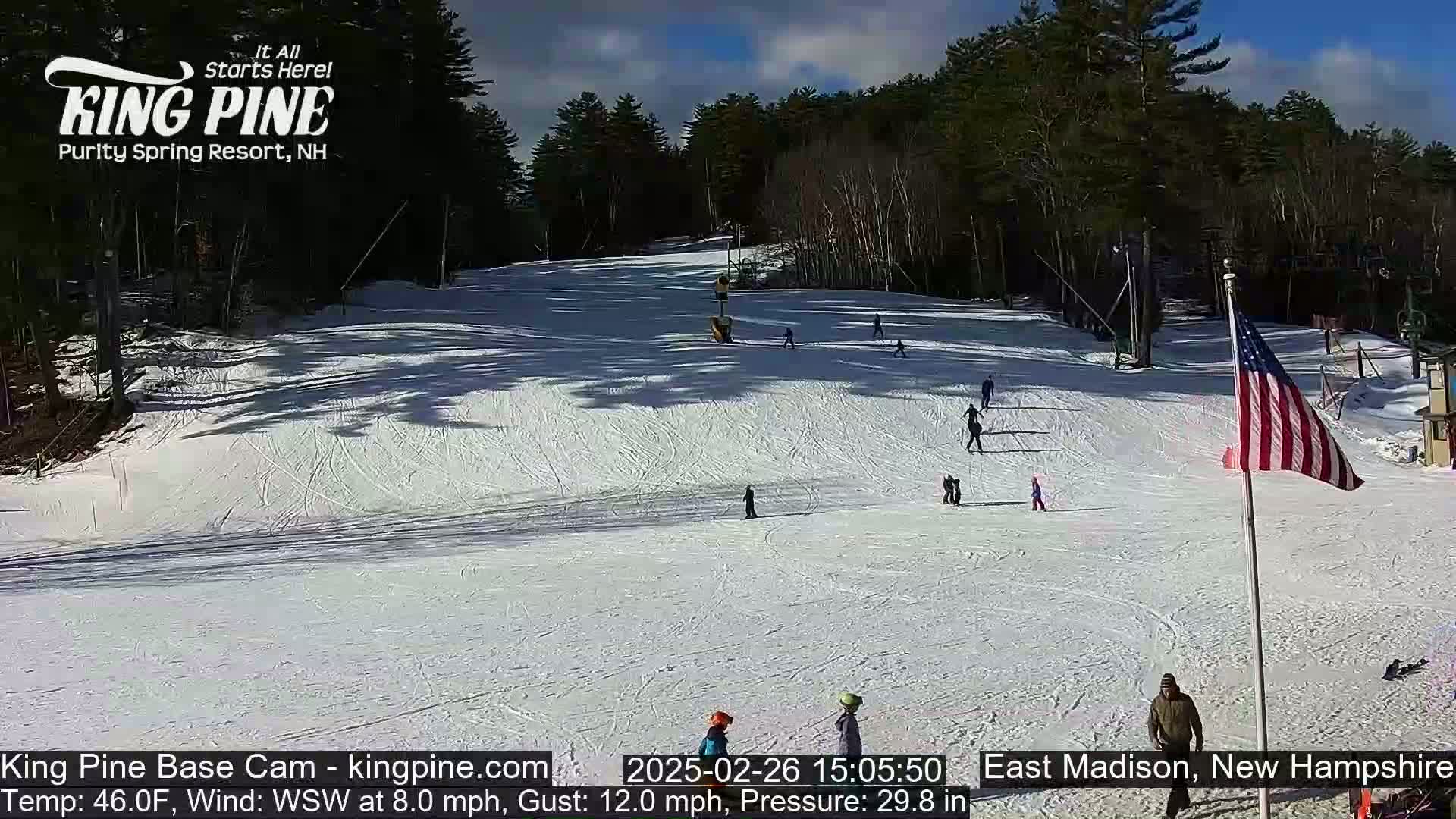 A snow-covered ski slope with several skiers and snowboarders, under a sunny sky.