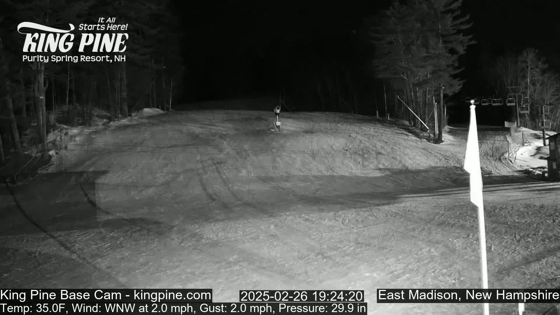 A nighttime, snow-covered ski slope is shown with a faint figure in the distance, under a clear sky, with a wind of 2 mph from the west-northwest.