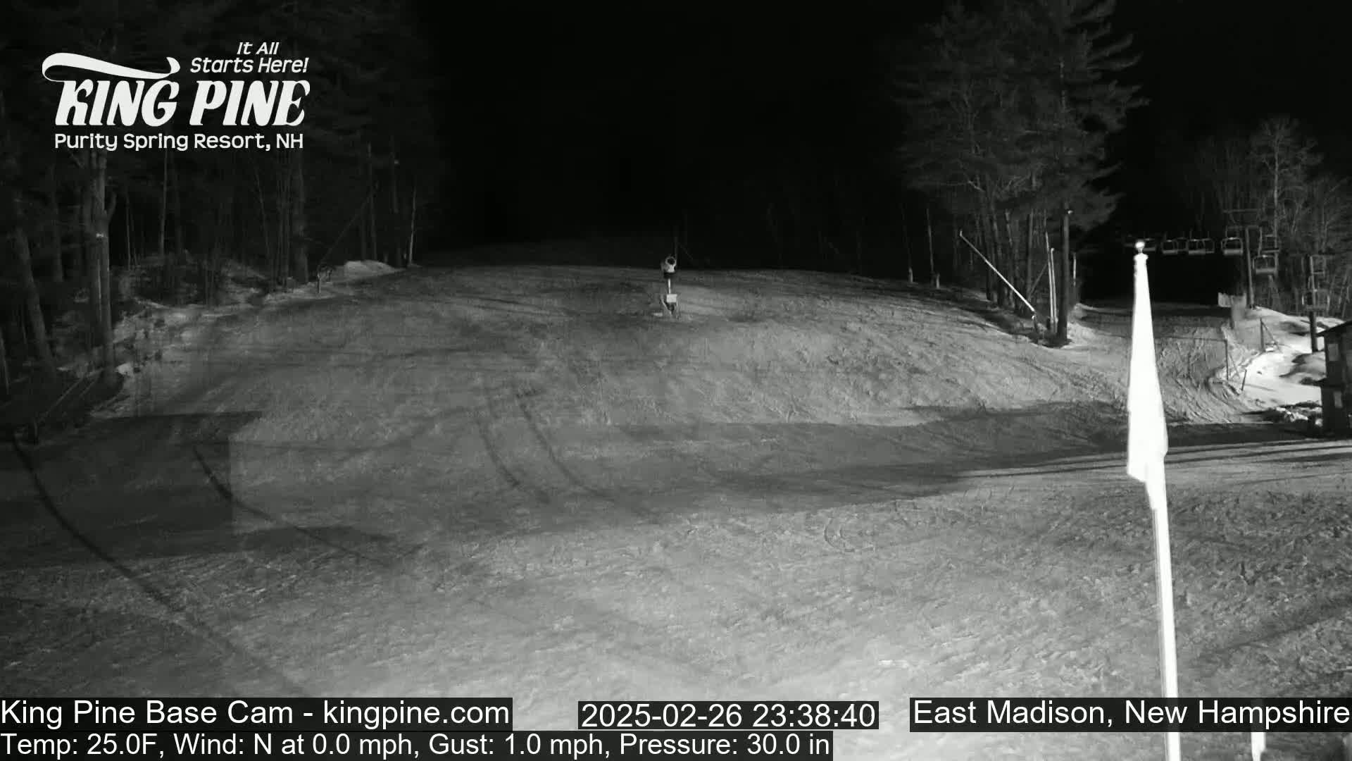 A nighttime, snow-covered ski slope is illuminated, showing a mostly empty hill with a single figure in the distance.