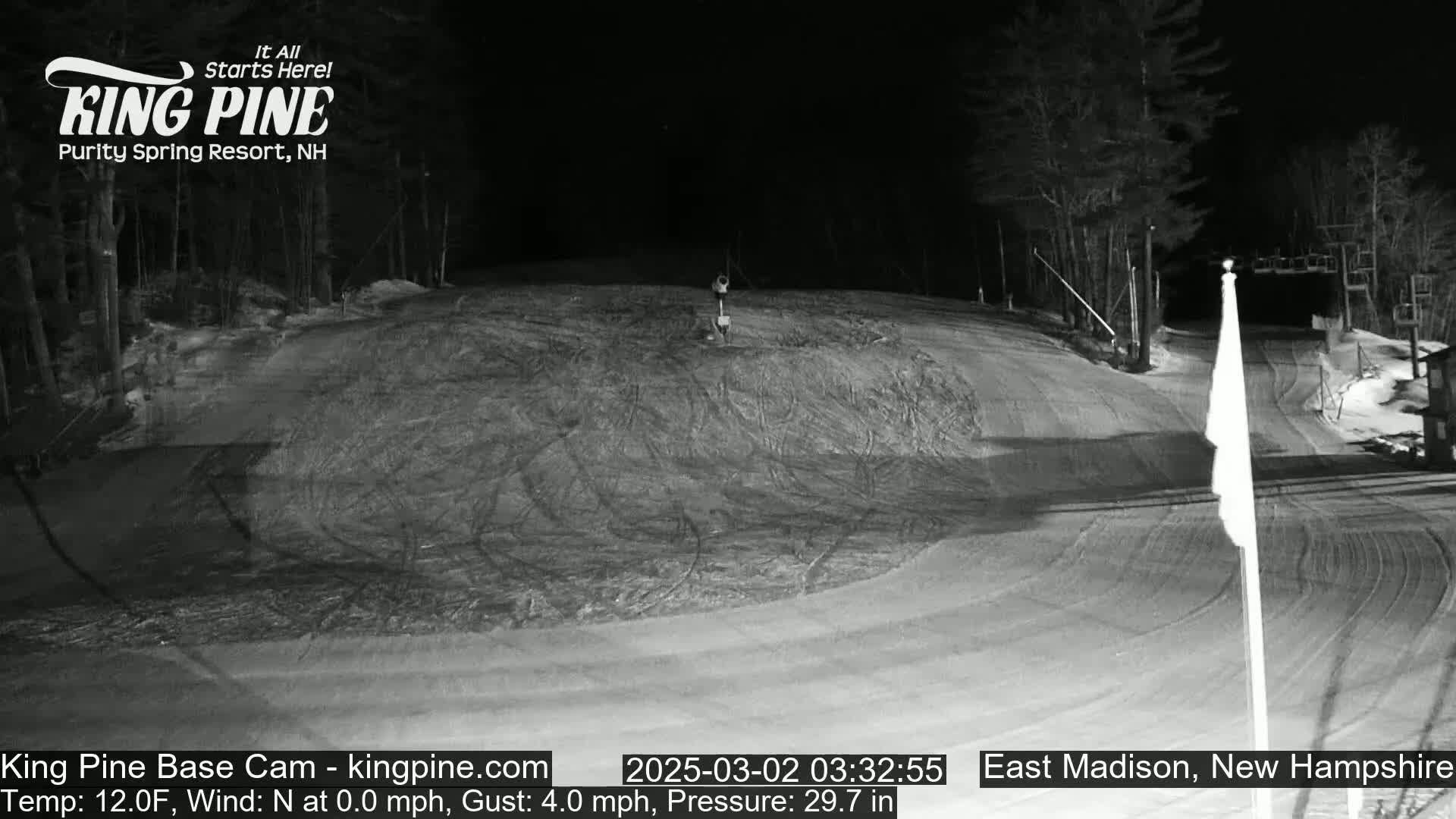 A nighttime view of a snow-covered ski slope with trees in the background under a dark sky.