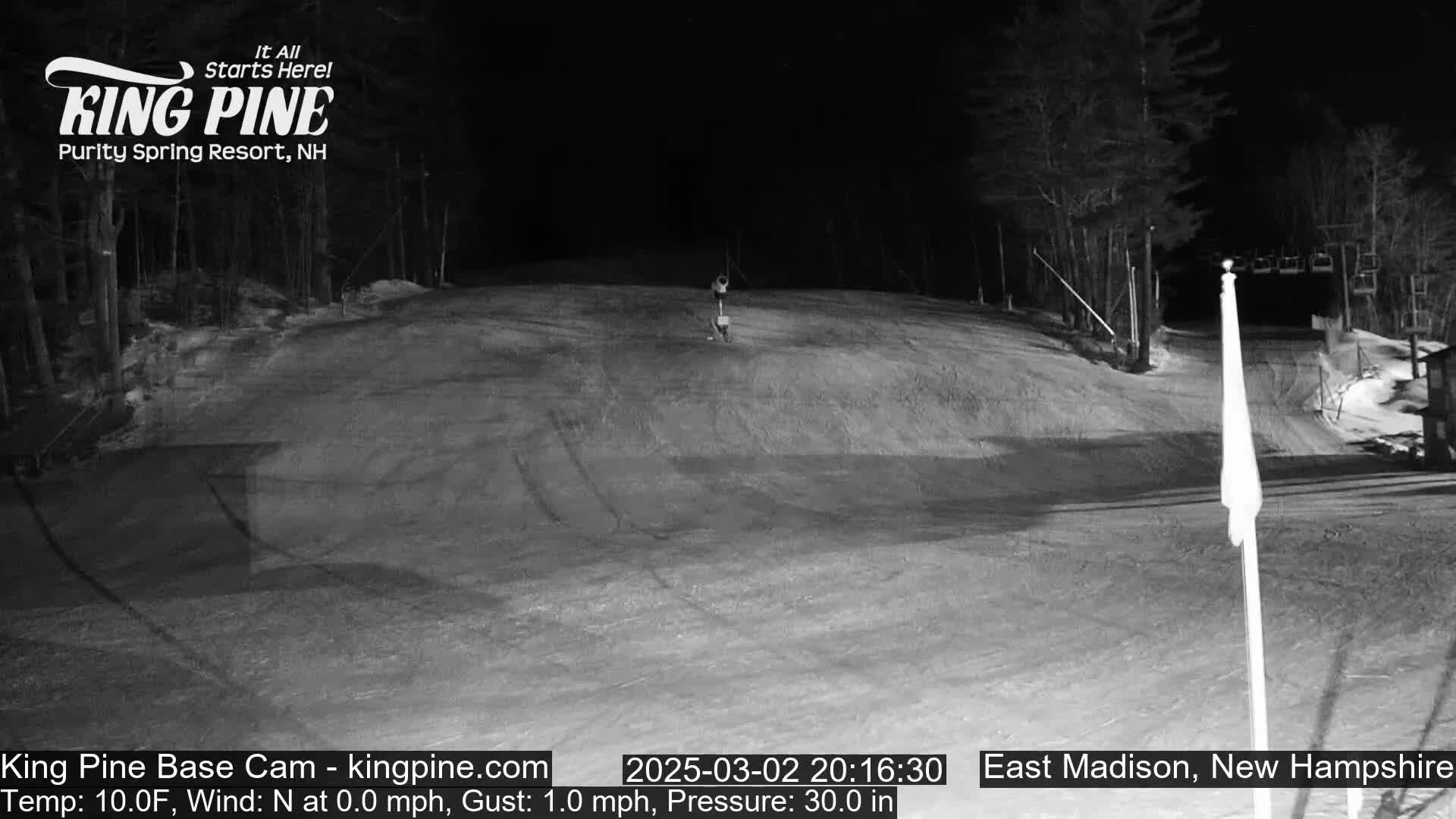 A nighttime, snow-covered ski slope is visible under a clear sky, with a lone figure skiing down a gently sloped section.