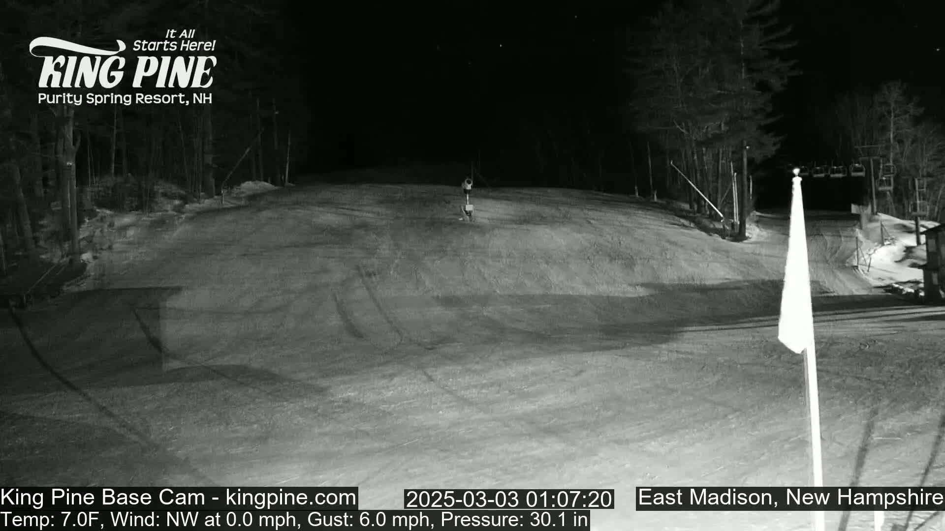 A nighttime, snow-covered ski slope is shown with a single person visible in the distance under a clear sky.