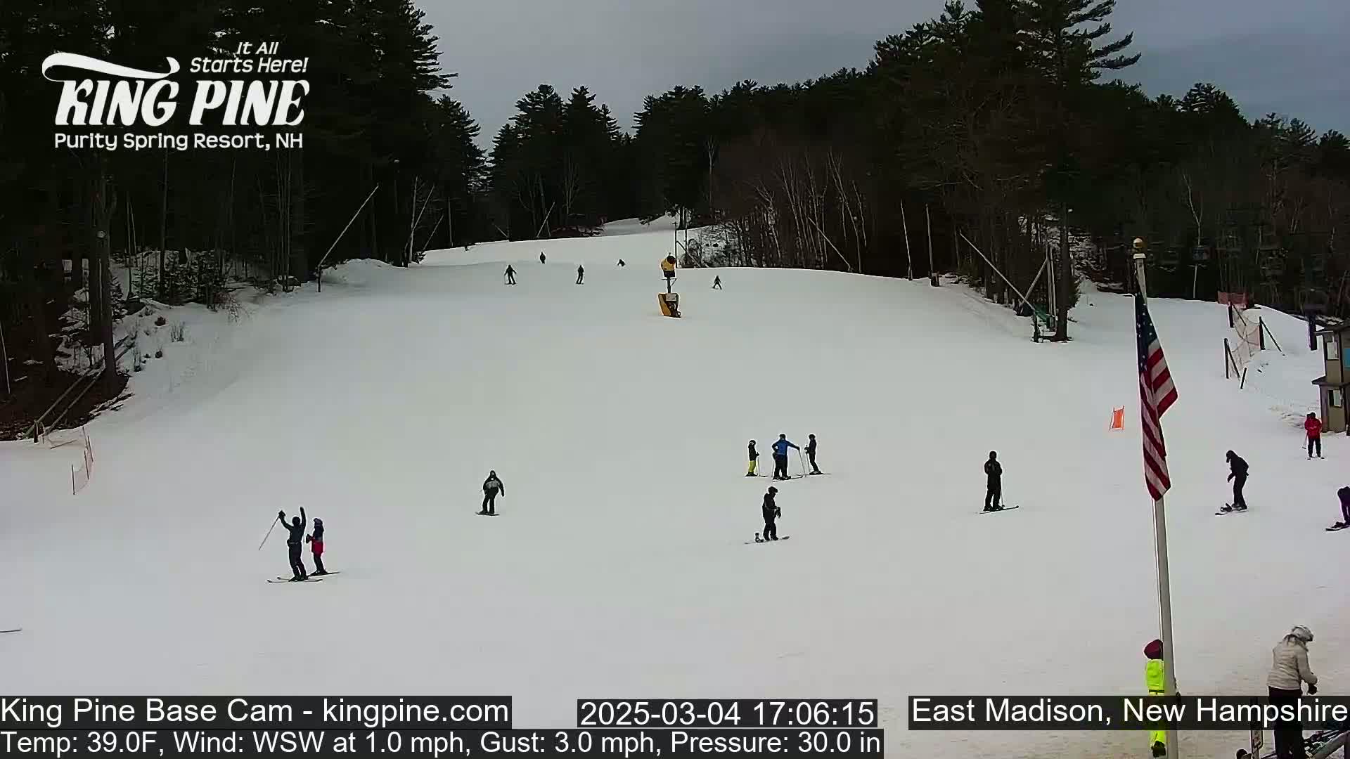 A snow-covered ski slope with several skiers and snowboarders, under an overcast sky.