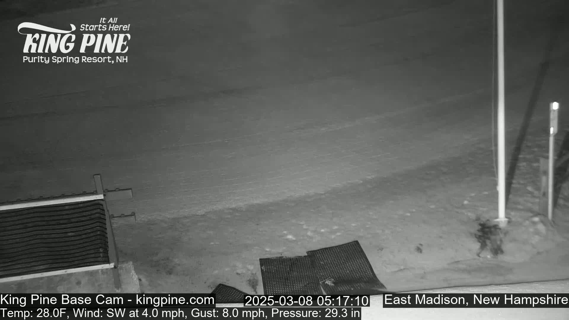 A nighttime, snow-covered scene shows a portion of a metal grate and some dark objects on the ground, under a southwest wind of 4 mph with gusts up to 8 mph.