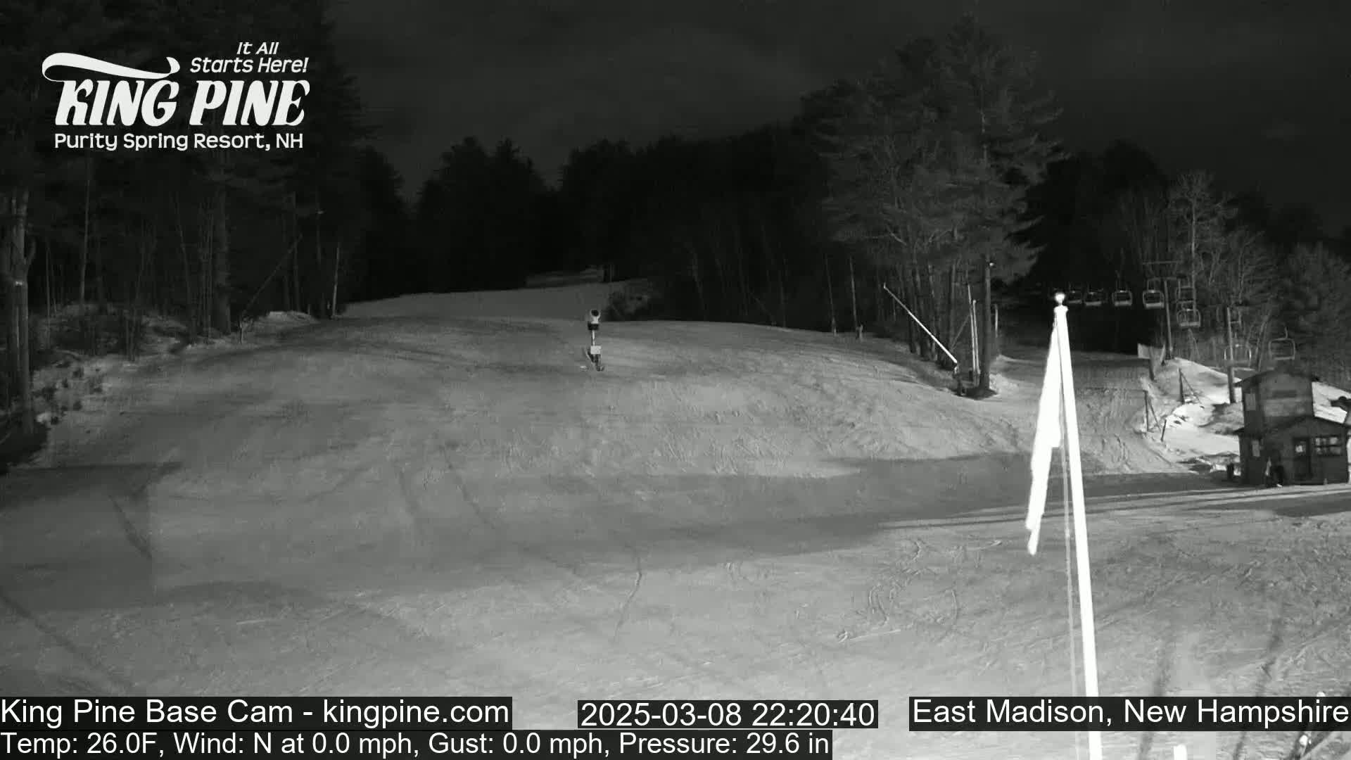 A nighttime, snow-covered ski slope is illuminated, with a single person visible in the distance.