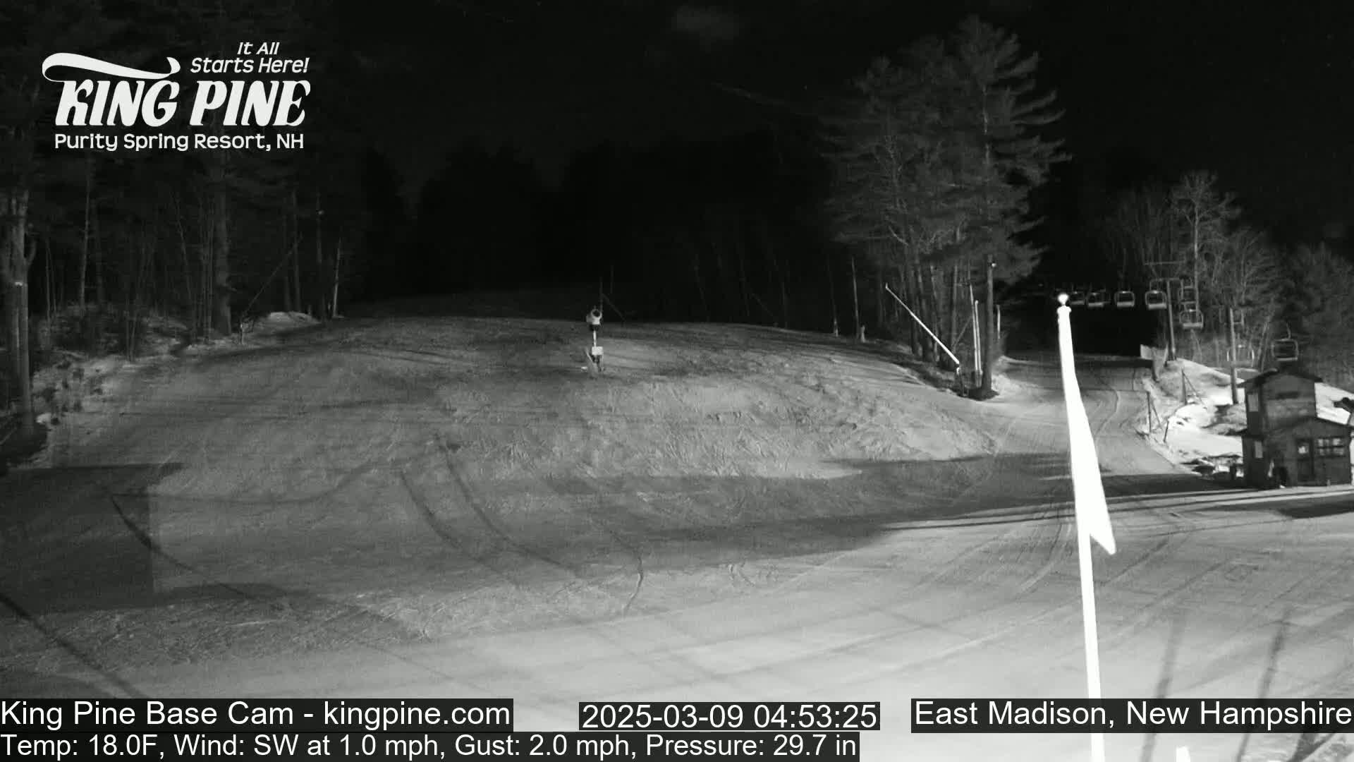 A nighttime view of a snow-covered ski slope with a few people visible, under a dark sky.