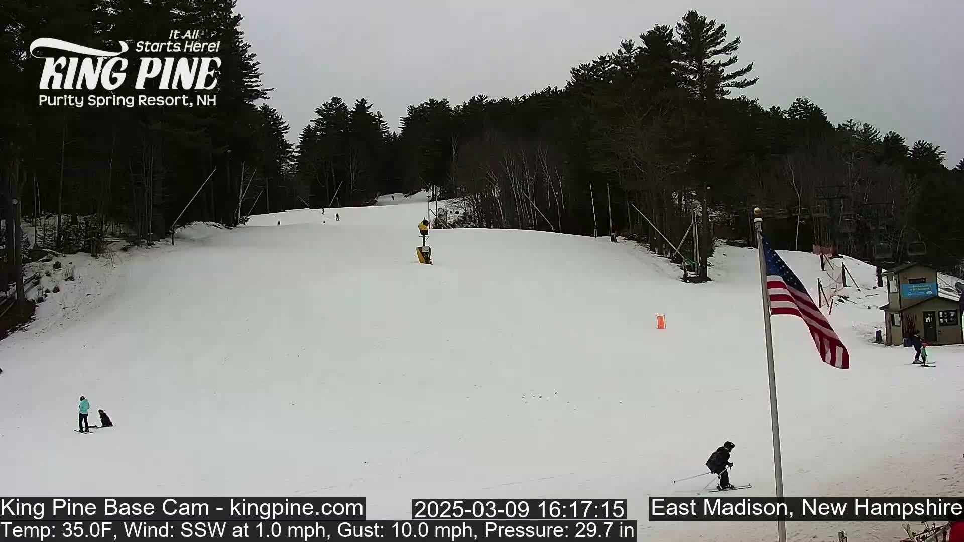 A snow-covered ski slope with several skiers and snowboarders, under an overcast sky.