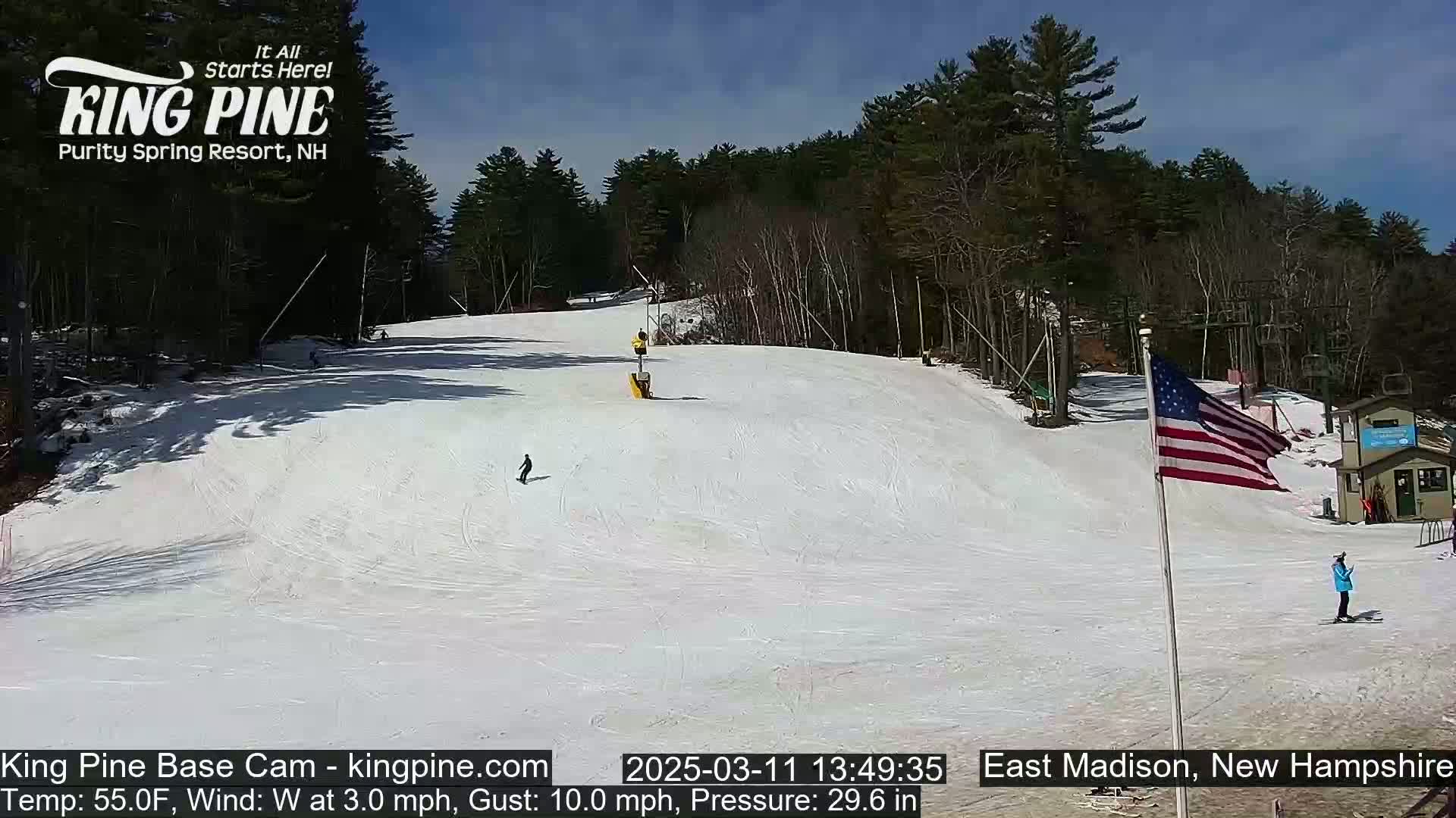 A snow-covered ski slope with several skiers and a chairlift is visible under a sunny sky.