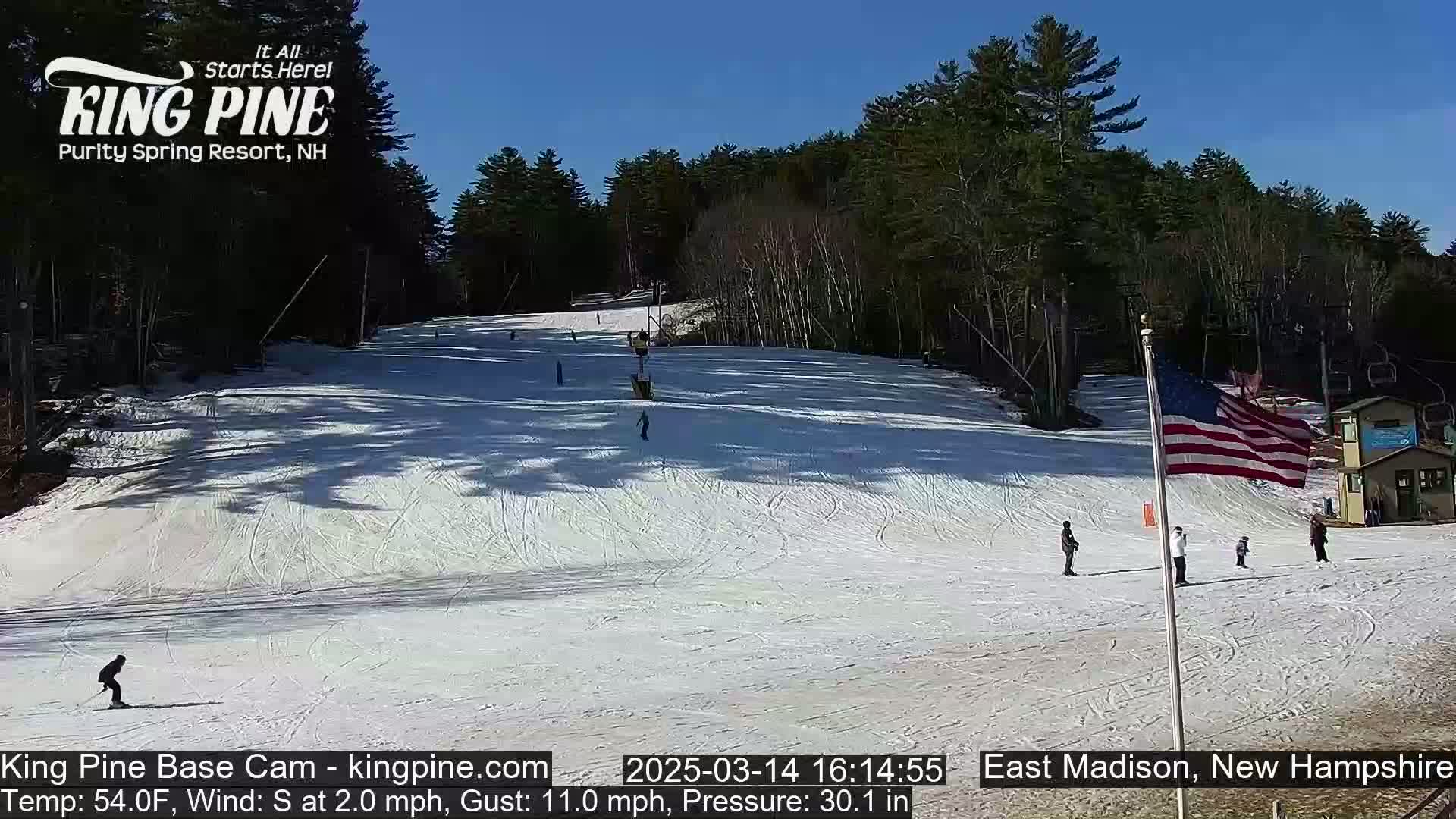 A snow-covered ski slope with several skiers and a ski lift is visible under a clear blue sky.
