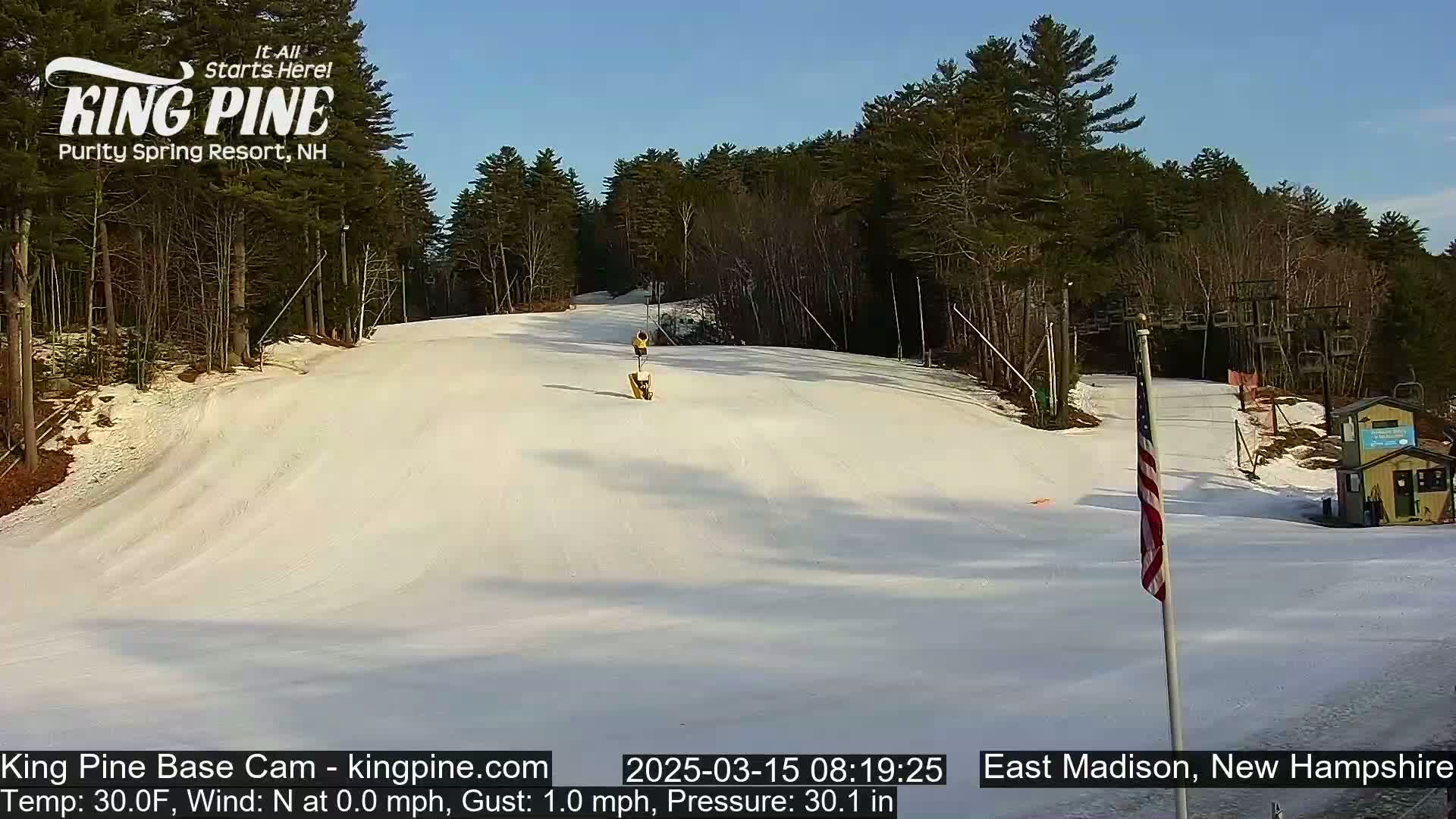 A snow-covered ski slope is visible, with a few people visible in the distance under a clear blue sky.
