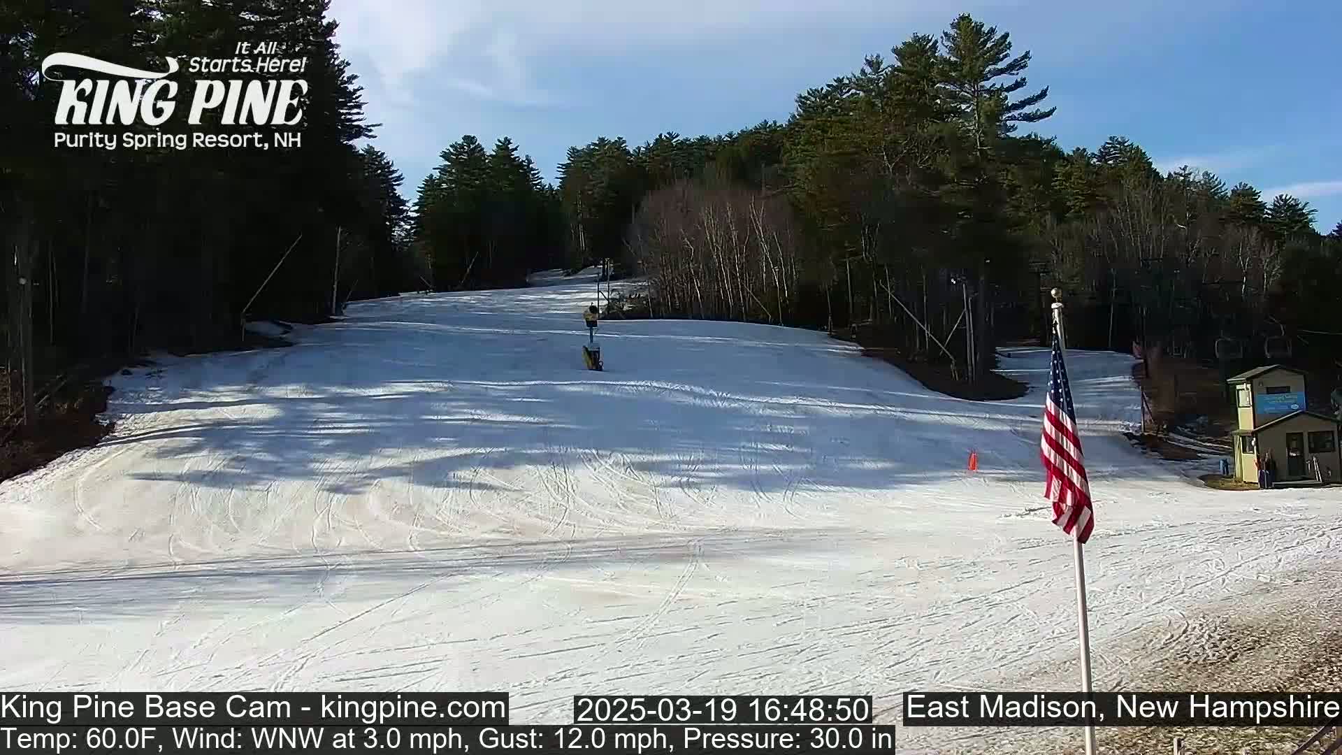 A snow-covered ski slope with a chairlift and an American flag is visible on a partly sunny day.