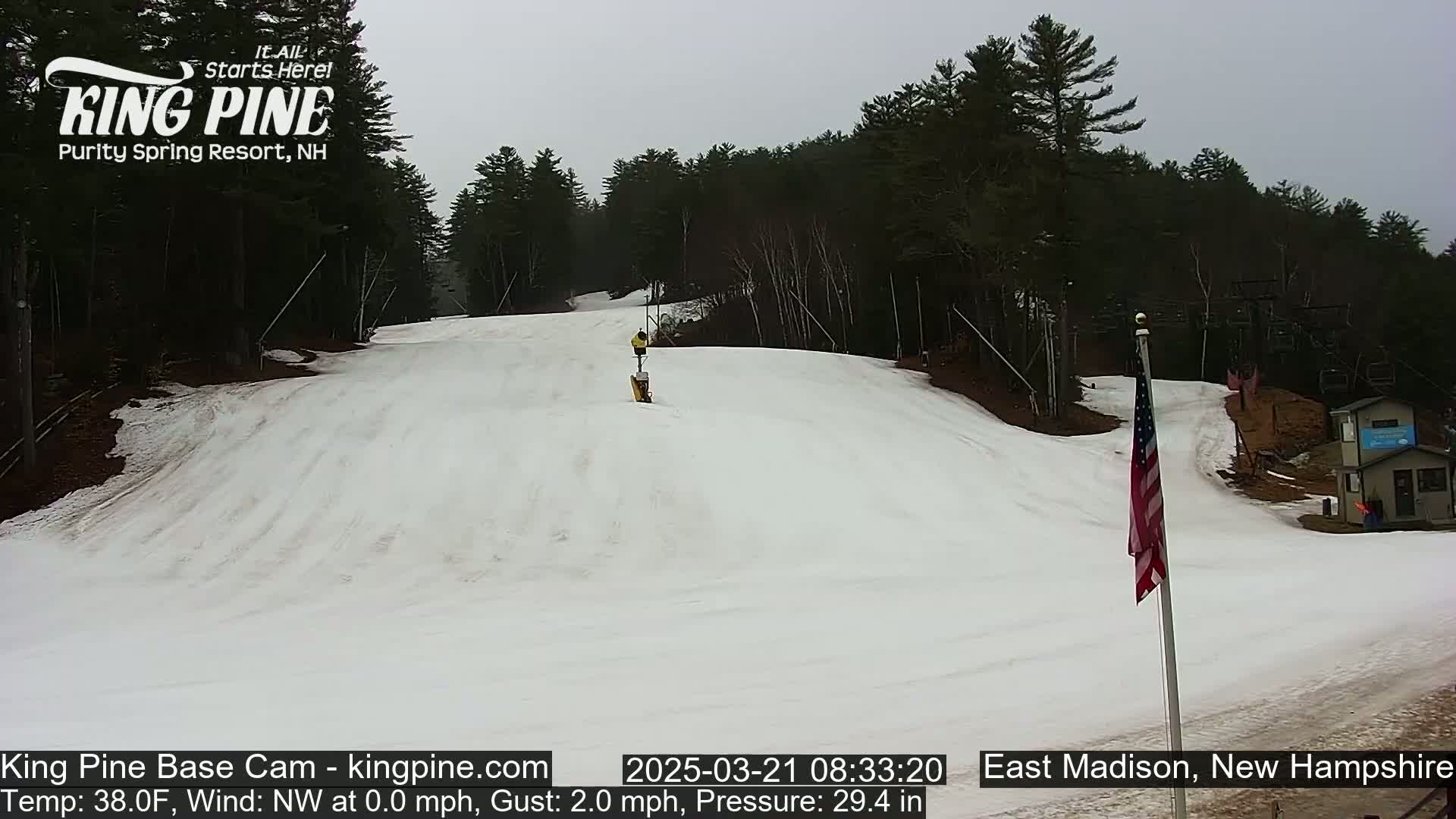 A snow-covered ski slope is visible, with a person visible in the distance, under an overcast sky.
