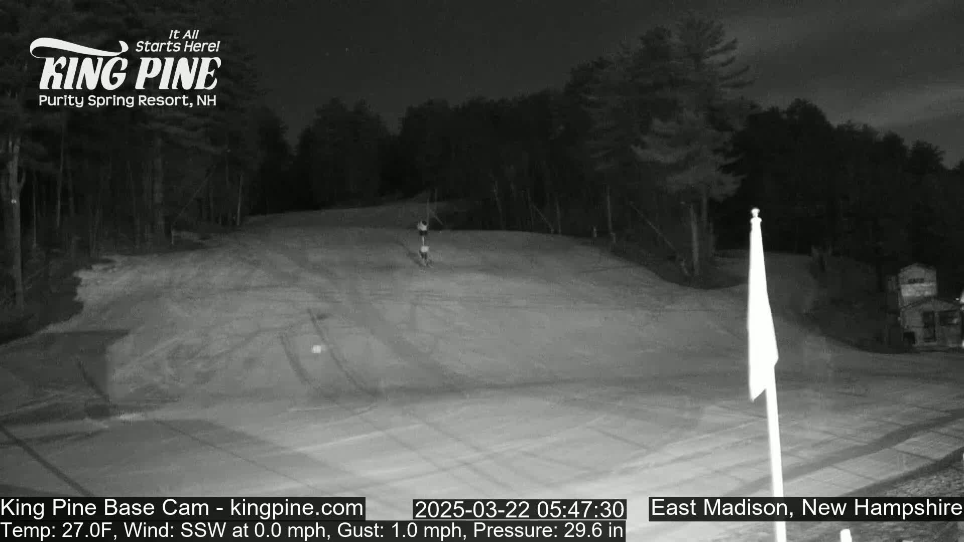 A nighttime, snow-covered ski slope is visible under a dark sky, with a single person skiing down it.