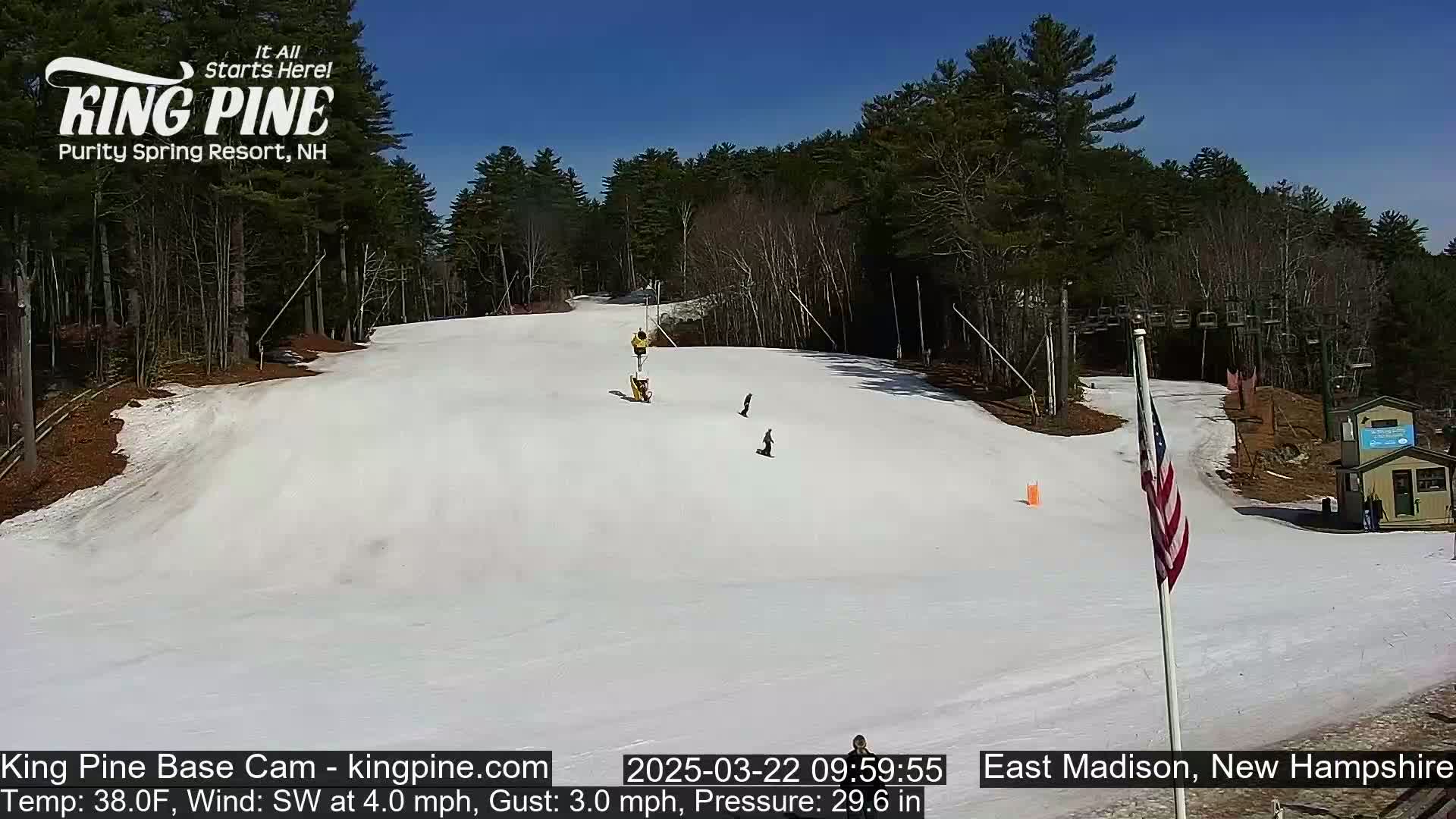 A snowy ski slope with several skiers and snowboarders under a clear blue sky.