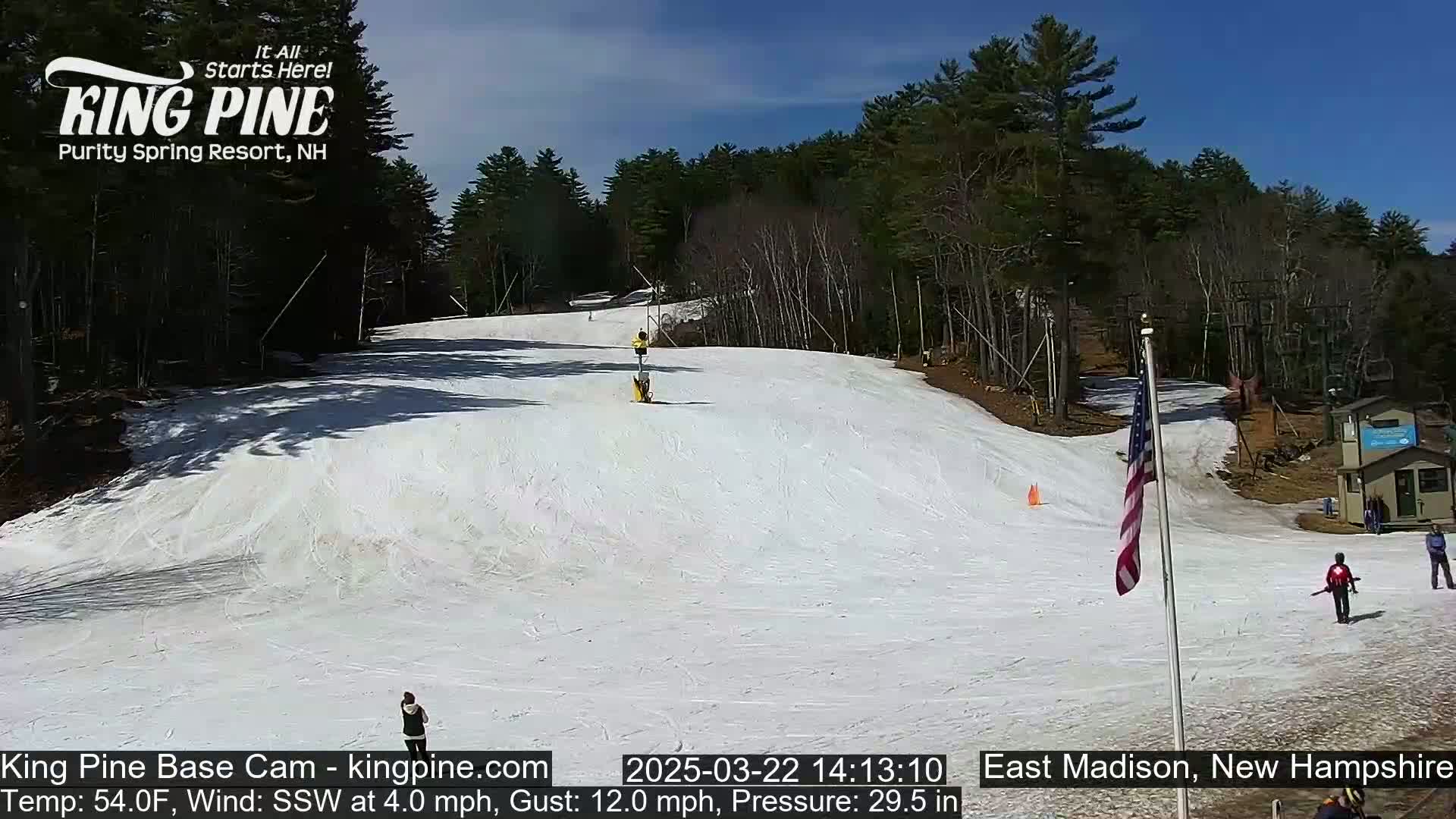 A snow-covered ski slope with a few skiers and a U.S. flag is visible under a sunny sky.