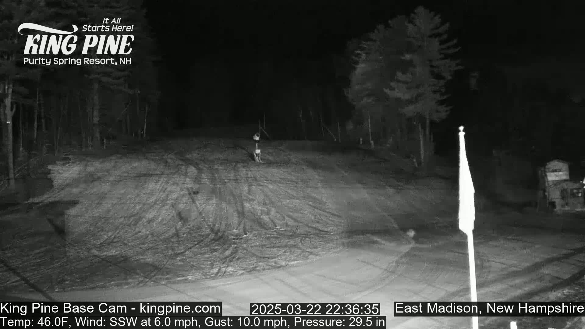 A nighttime, snow-covered ski slope is visible, with trees lining the sides and a flagpole in the lower right.