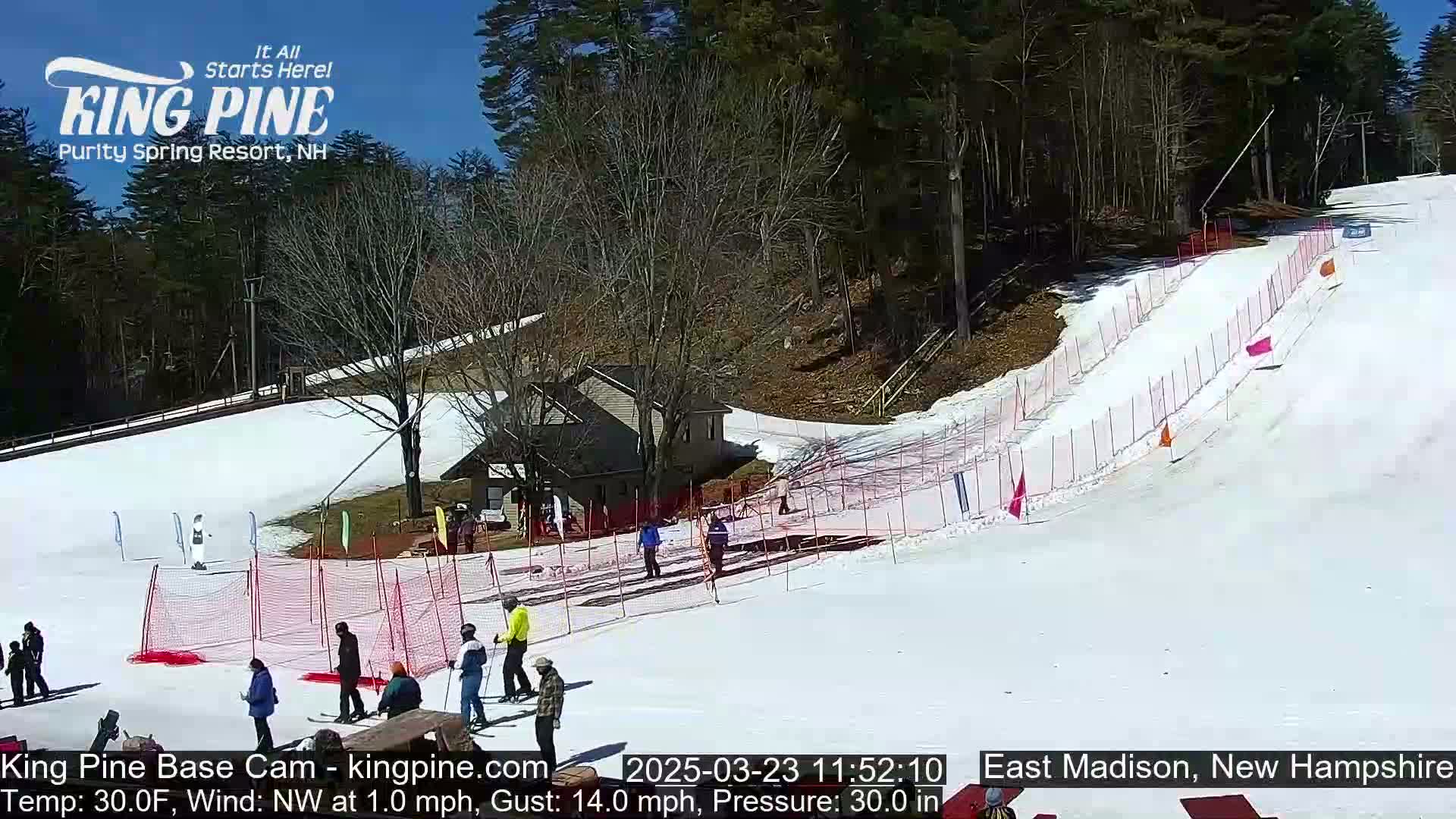 A snow-covered ski slope with several skiers and spectators, under a sunny sky.