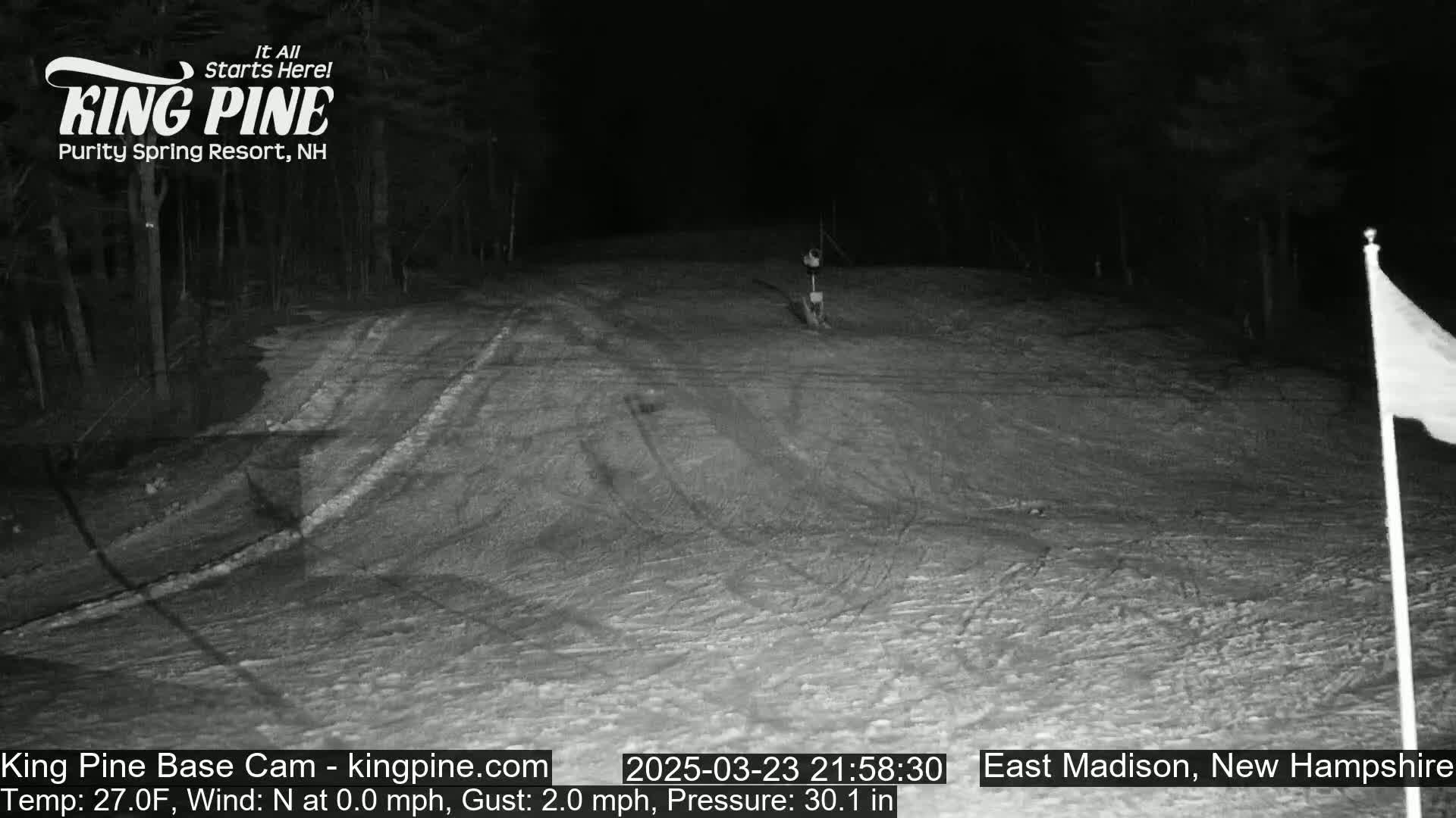 A nighttime, snow-covered slope is visible under a dark sky with a calm wind.