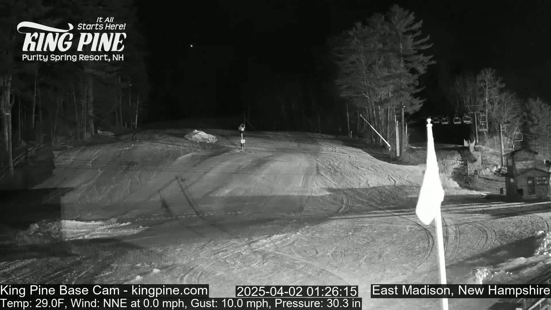 A nighttime, snow-covered ski slope is mostly empty under a clear sky.