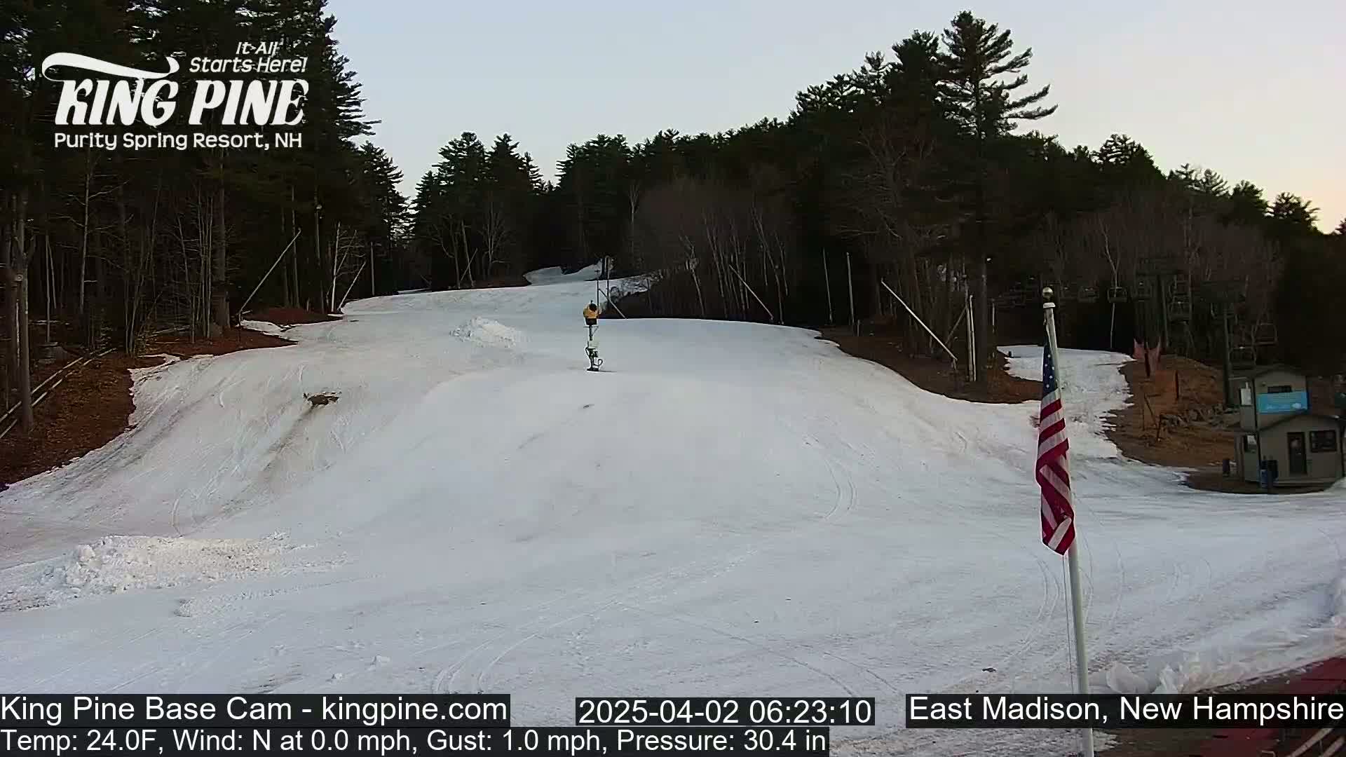 A skier descends a snow-covered slope in a wooded area under a twilight sky.