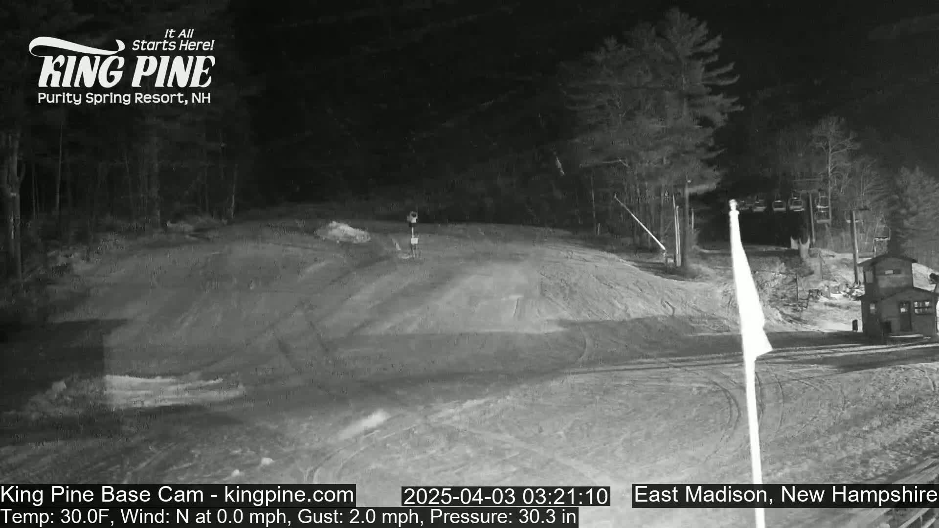 A nighttime view of a snow-covered ski slope with a ski lift and a small building in the background.