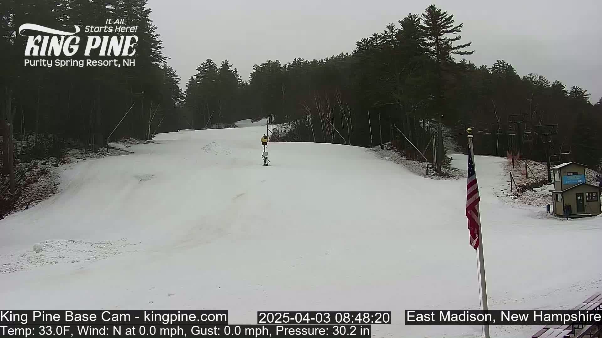 A snow-covered ski slope with a person skiing down it, under an overcast sky.