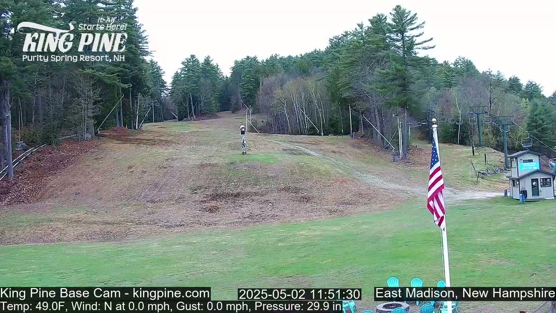 A ski slope with a chairlift and an American flag, surrounded by trees under a mostly clear sky.