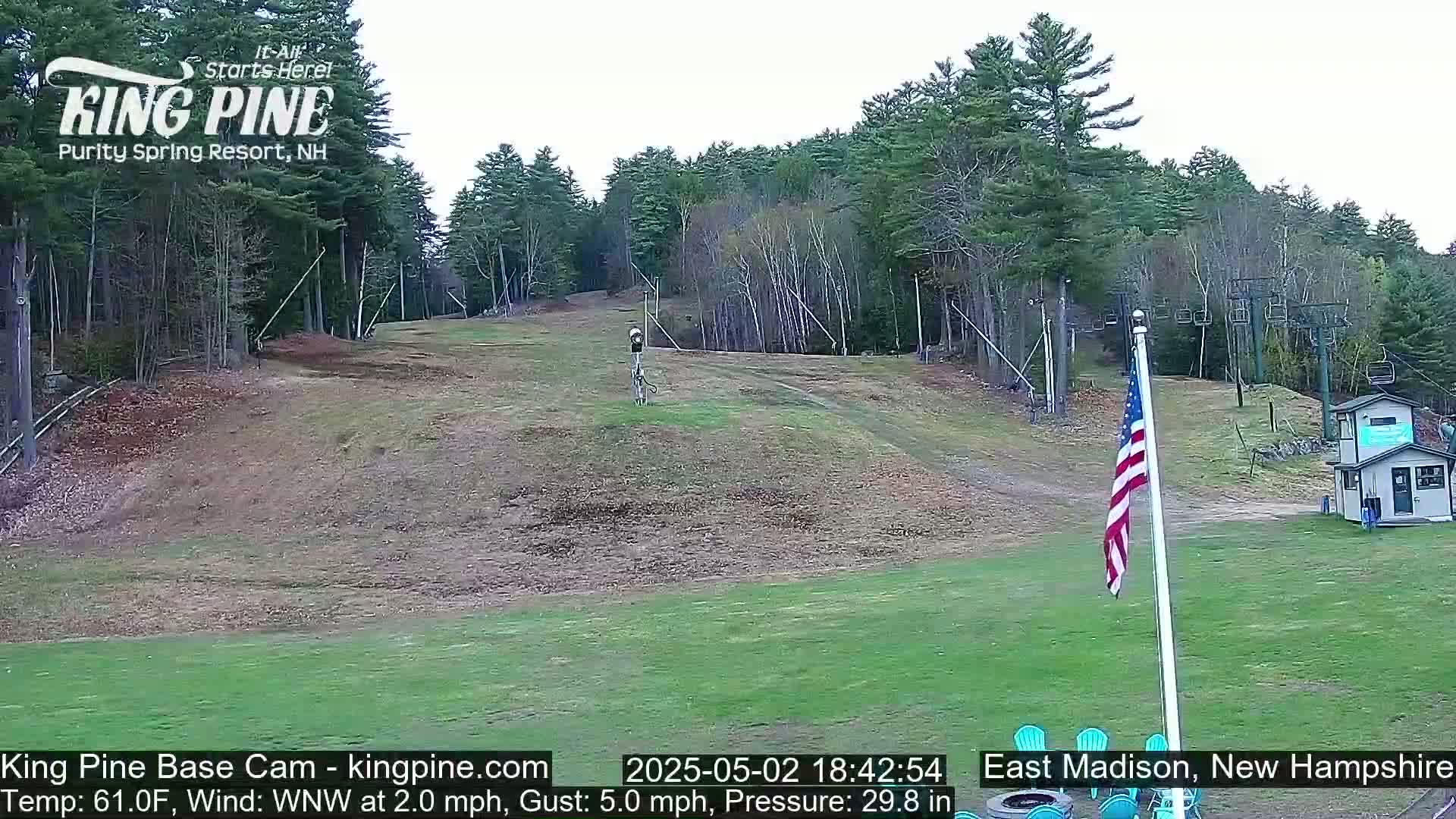 A grassy ski slope with a chairlift and an American flag, surrounded by trees under an overcast sky.