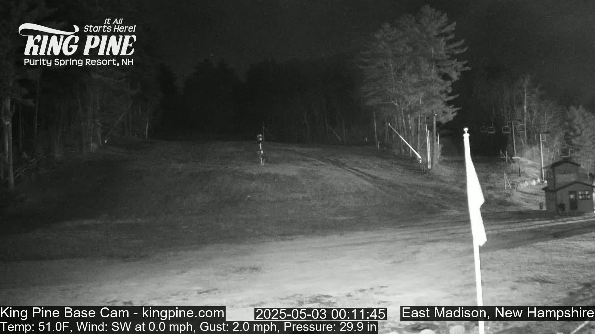 A nighttime, low-light view of a snow-covered hill with trees and a flagpole in the foreground.