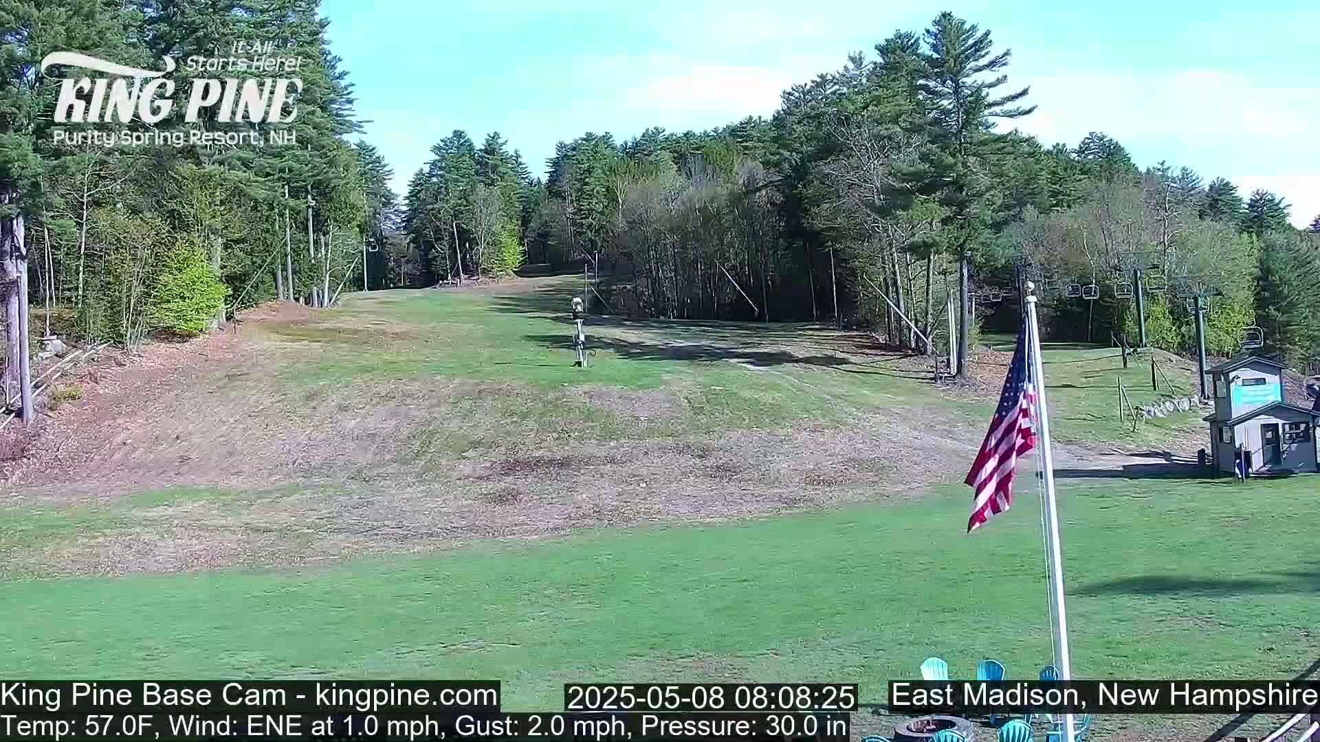 A grassy ski slope with a chairlift and American flag is visible under a mostly sunny sky.