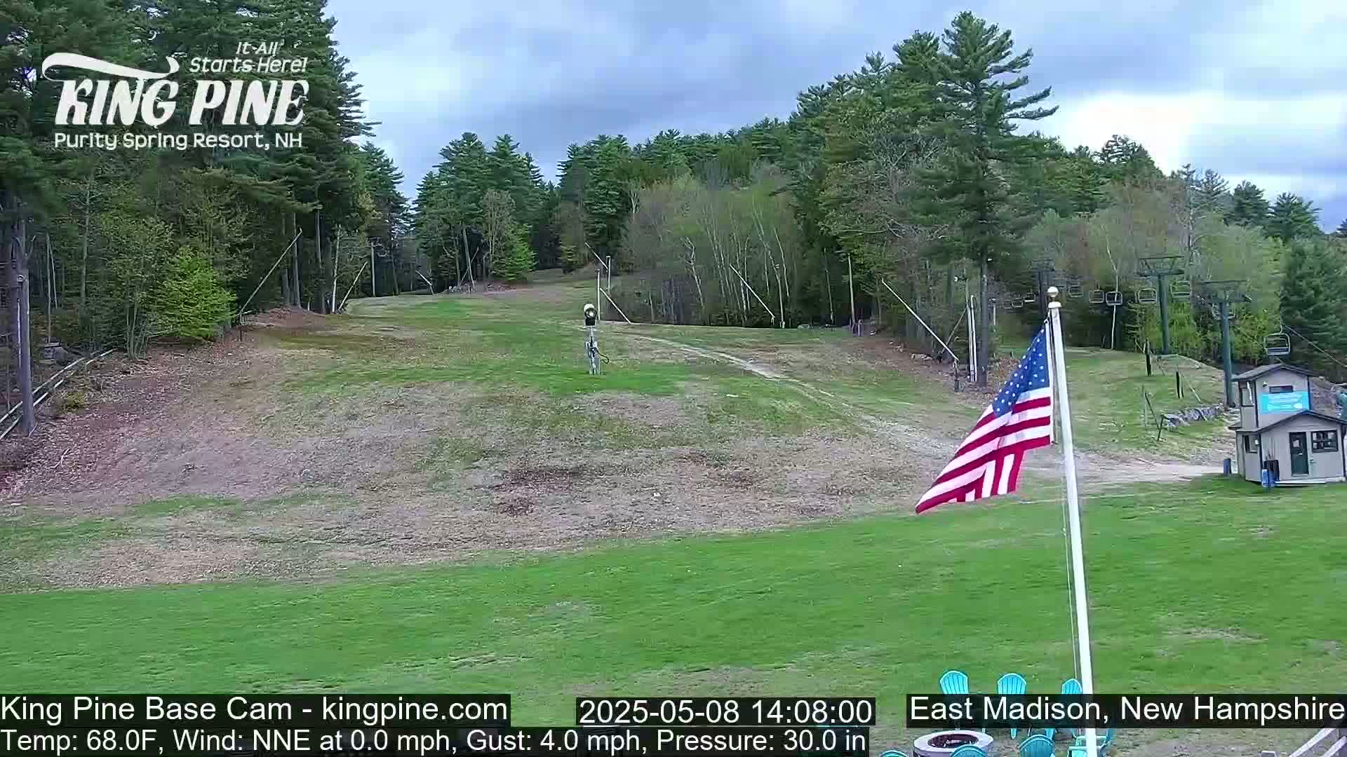 A grassy ski slope with a chairlift and an American flag is visible under a partly cloudy sky.