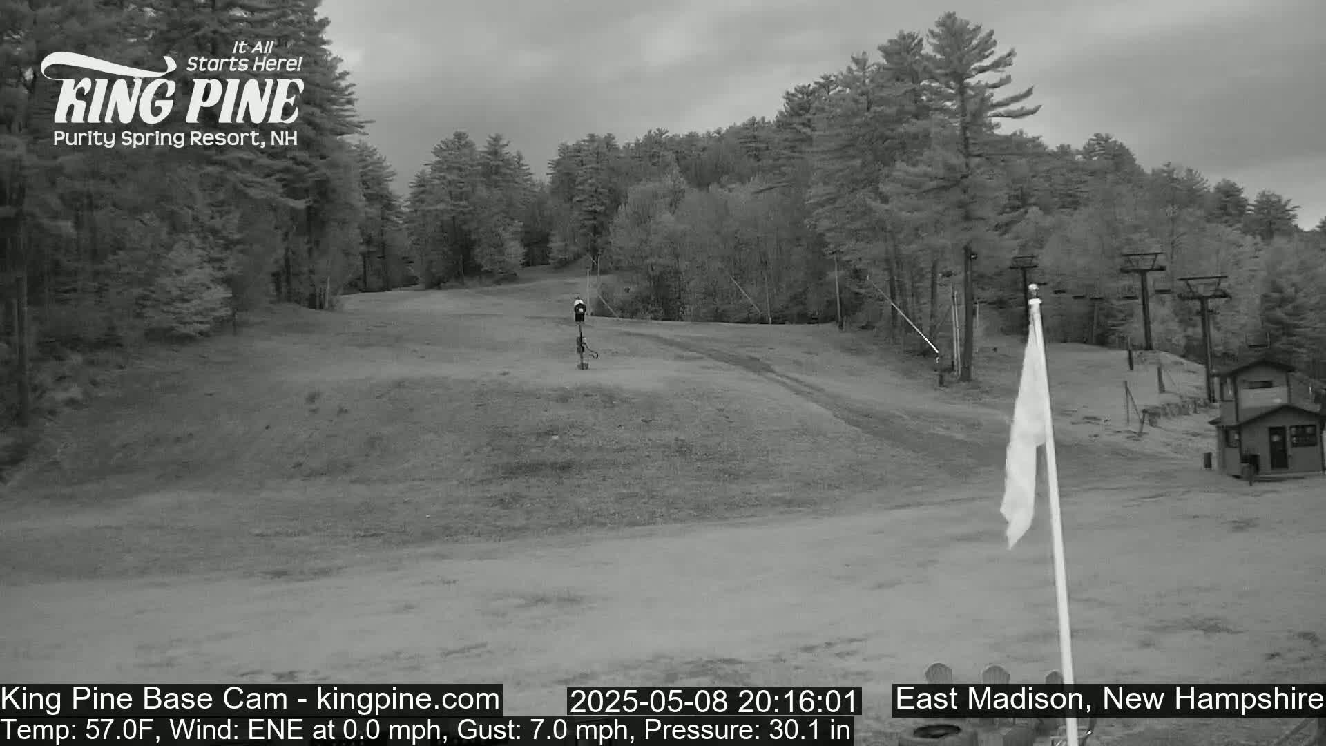 A mostly cloudy, gray day at a ski resort shows a mostly empty ski slope with a chairlift in the background.