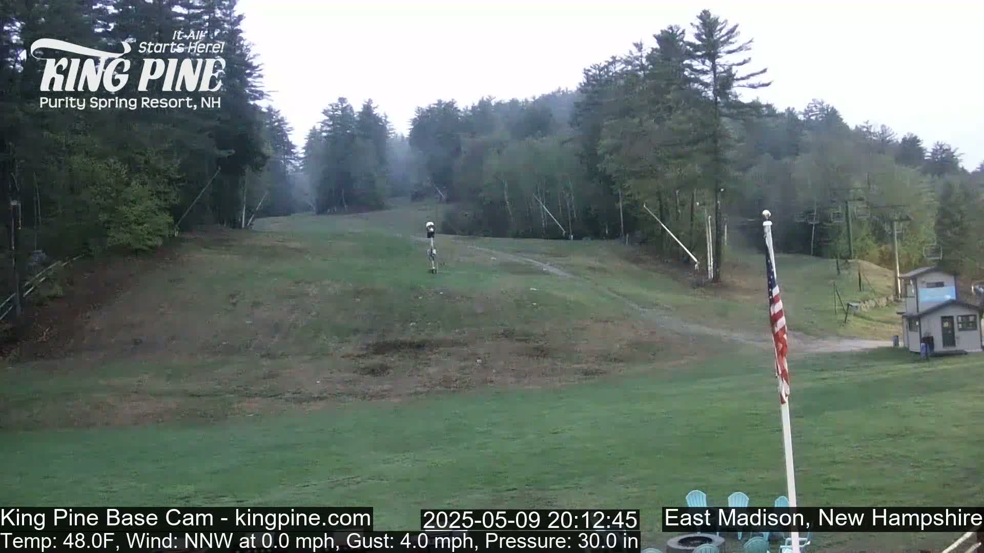A grassy ski slope is visible, surrounded by trees under an overcast sky.