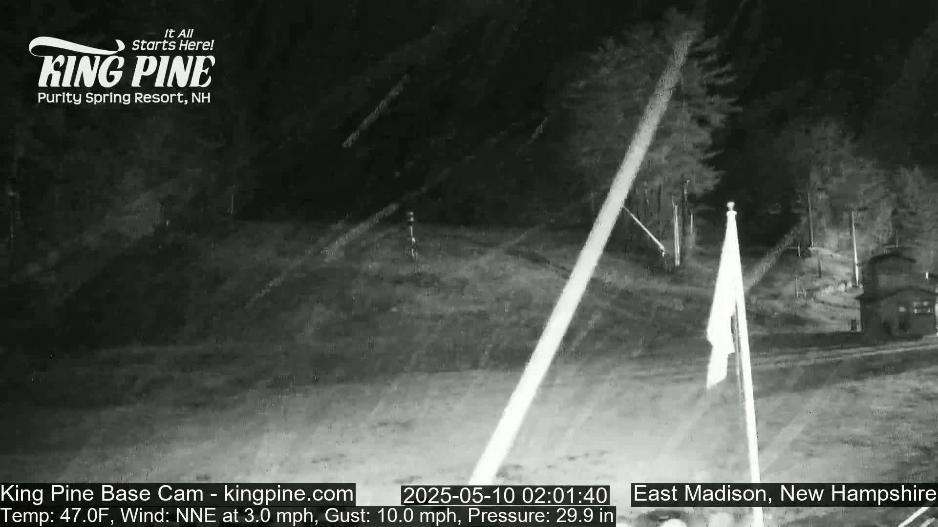 A nighttime, low-light outdoor scene shows a mostly empty road, some trees, and a flagpole with a flag in the wind.