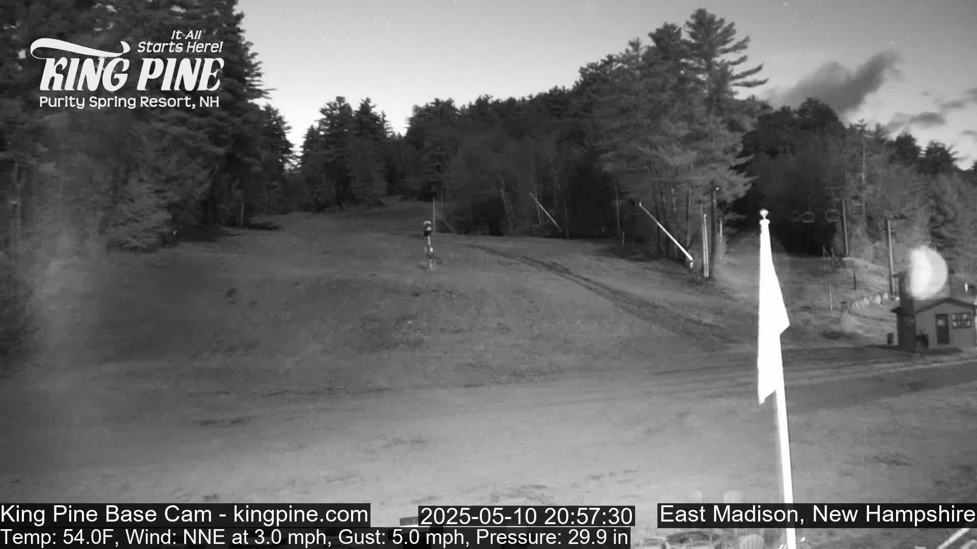 A nighttime view of a mostly empty ski slope with trees in the background under a partly cloudy sky.