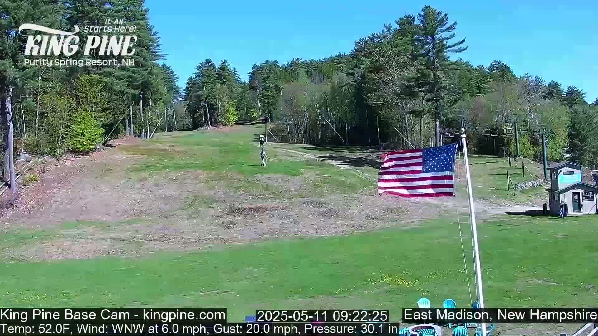 A grassy ski slope with a chairlift and an American flag waving under a clear blue sky.