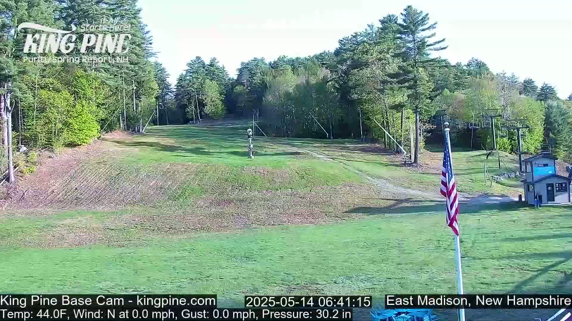 A grassy ski slope with a chairlift and an American flag is visible on a clear, sunny day.