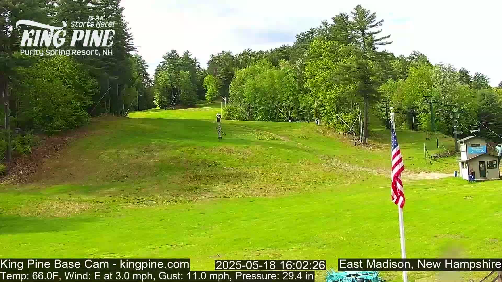 A grassy hill with a ski lift in the background on a partly sunny day with a light east wind.