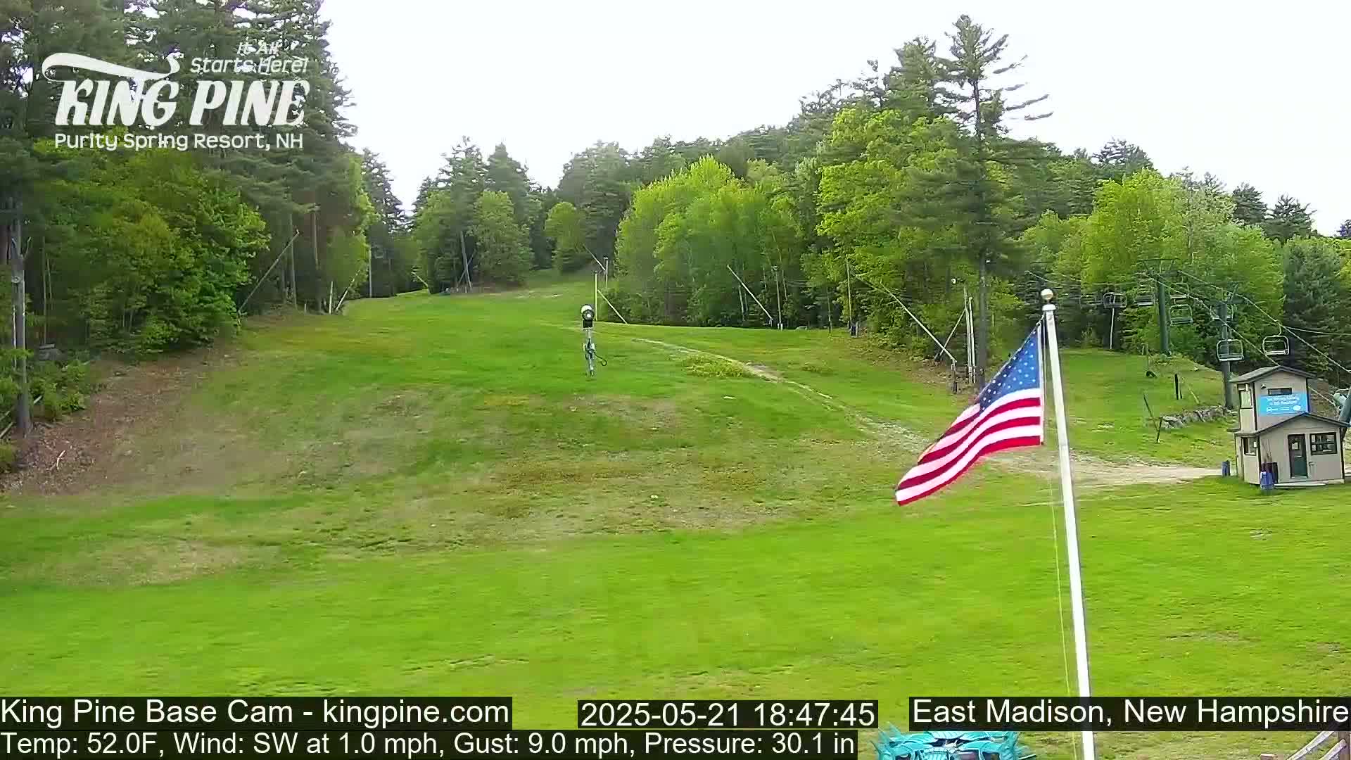 A grassy ski slope with a chairlift and American flag is visible under a partly cloudy sky.