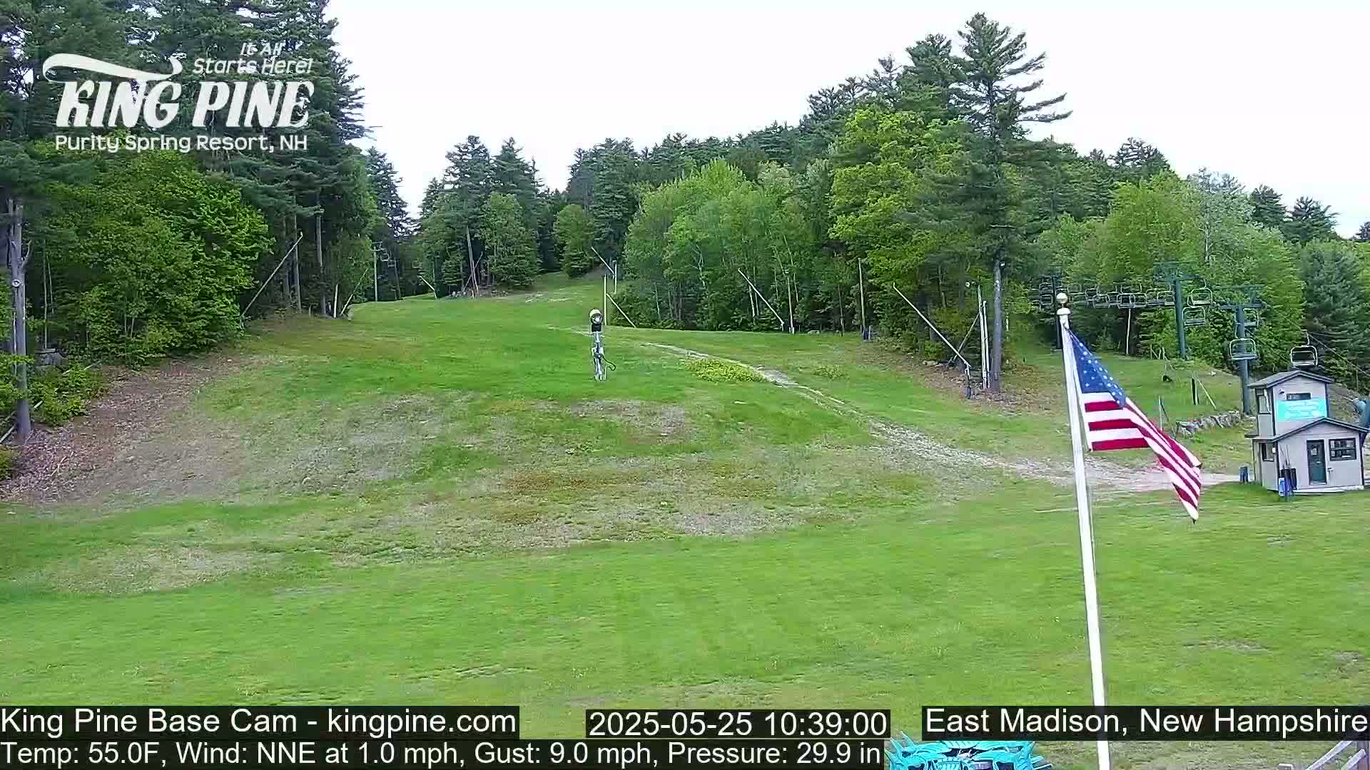 A grassy ski slope with a chairlift and an American flag, under a mostly clear sky.