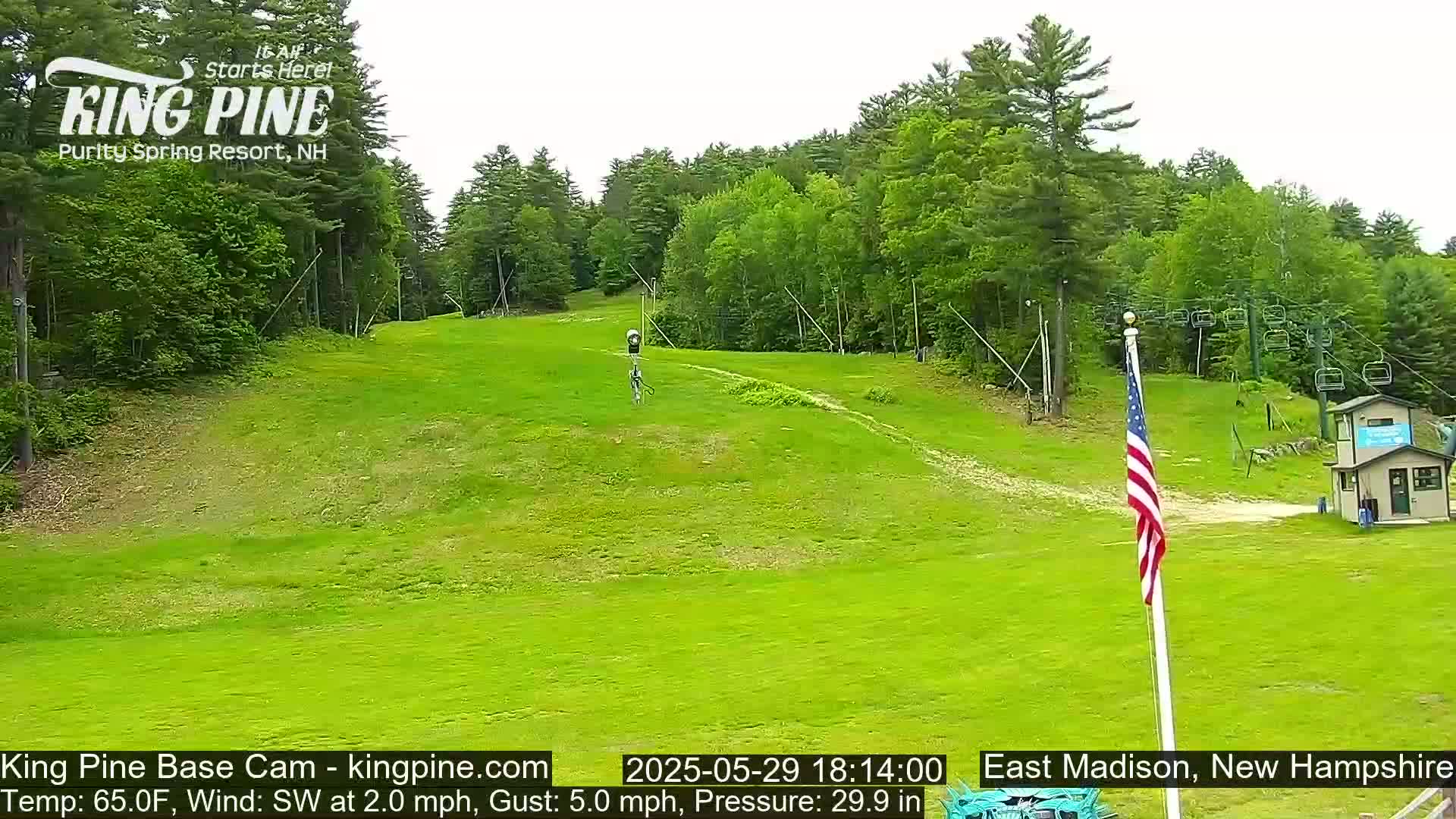 A grassy ski slope is visible, with a chairlift and a small building in the background, under partly cloudy skies.