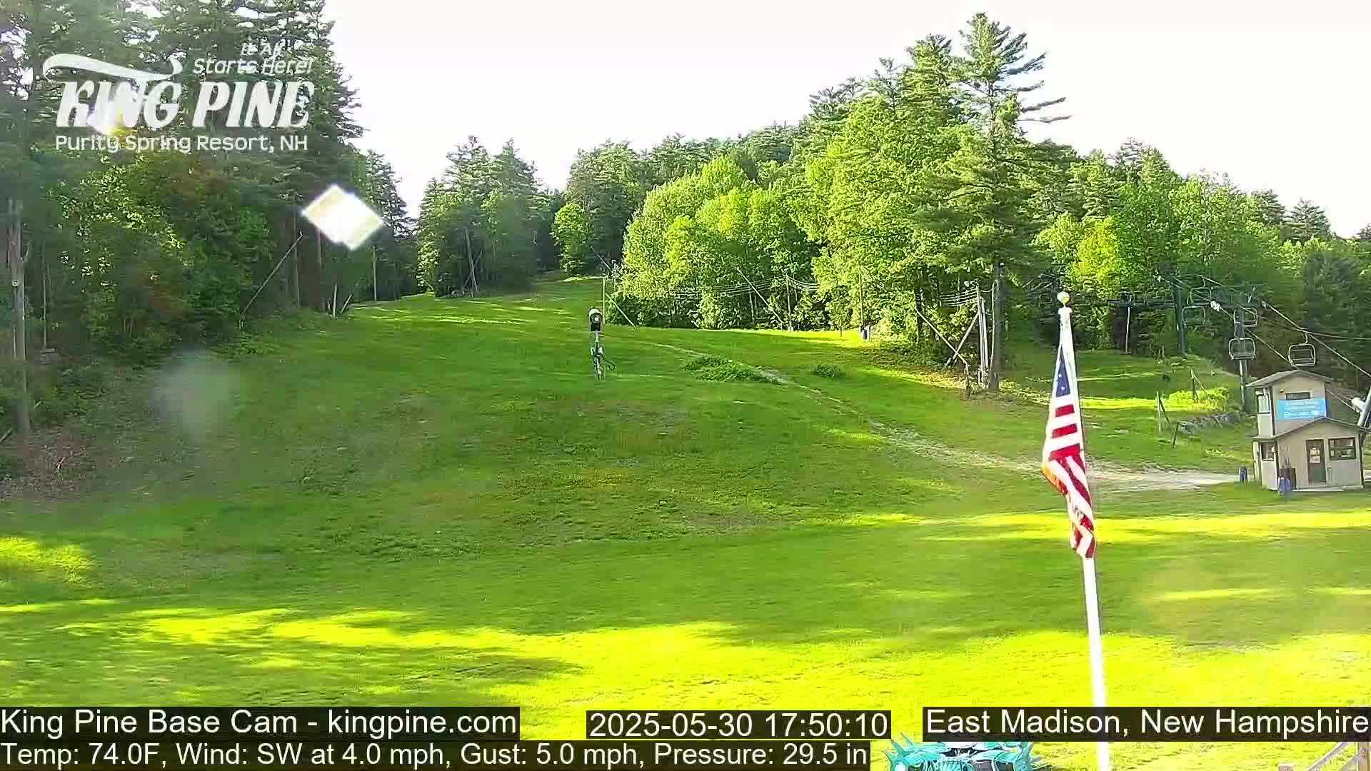A grassy hill with a ski lift and an American flag, under a mostly clear sky.
