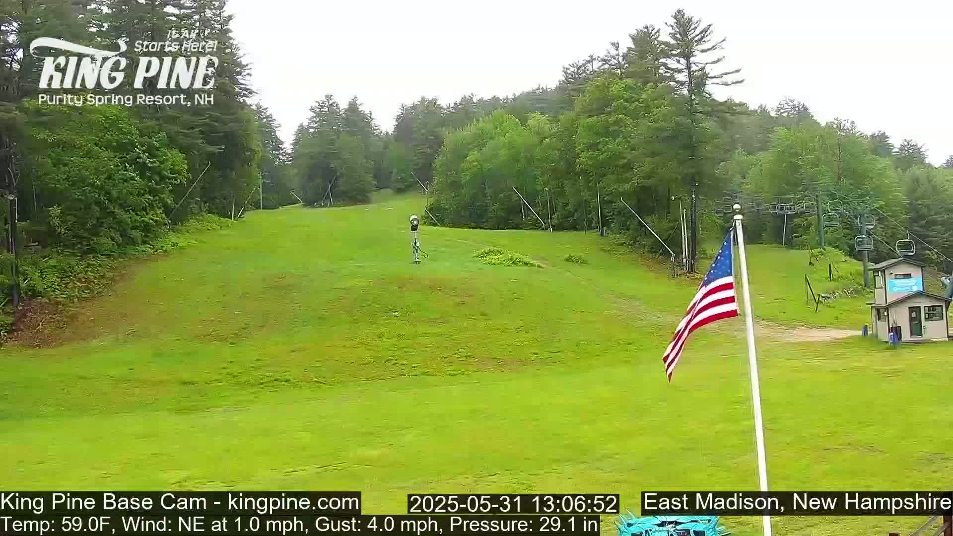 A grassy ski slope with a chairlift and an American flag is visible under overcast skies.