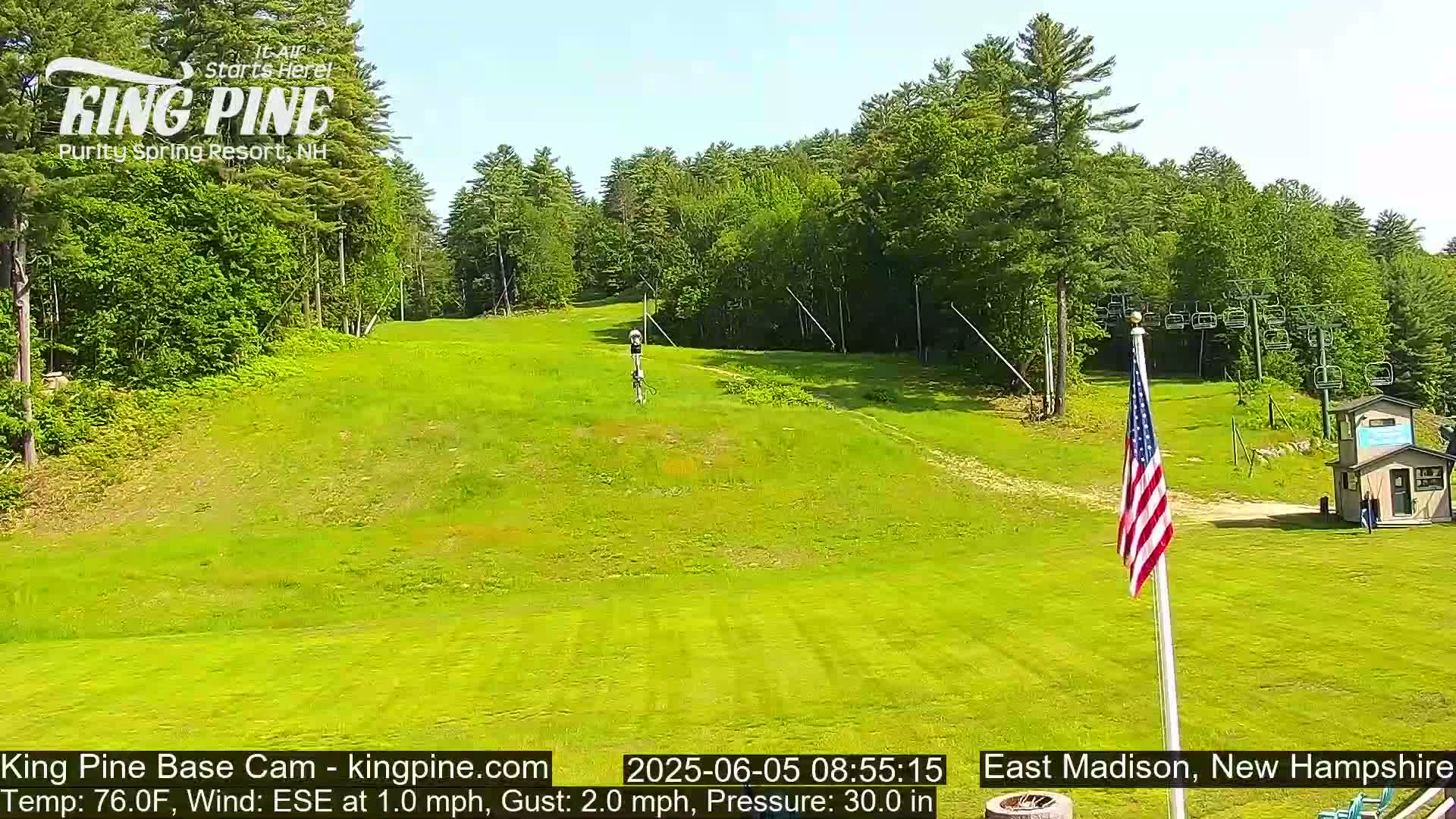 A grassy hill with a ski lift and a US flag is visible, under a clear sunny sky.