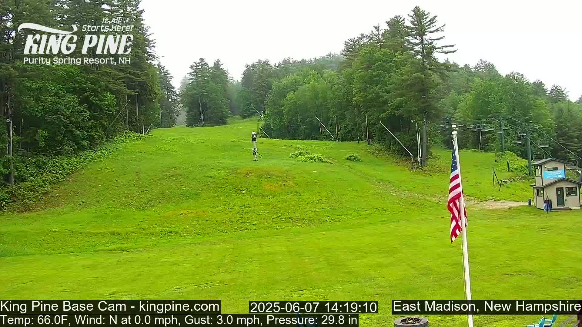 A grassy ski slope with a chairlift and American flag is visible on an overcast day.