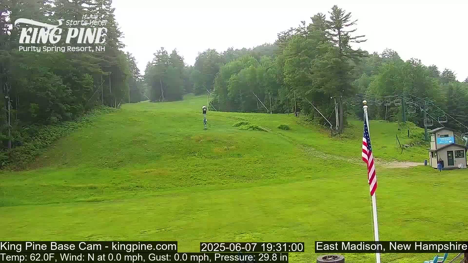 A grassy ski slope with a chairlift and an American flag is visible on an overcast day.